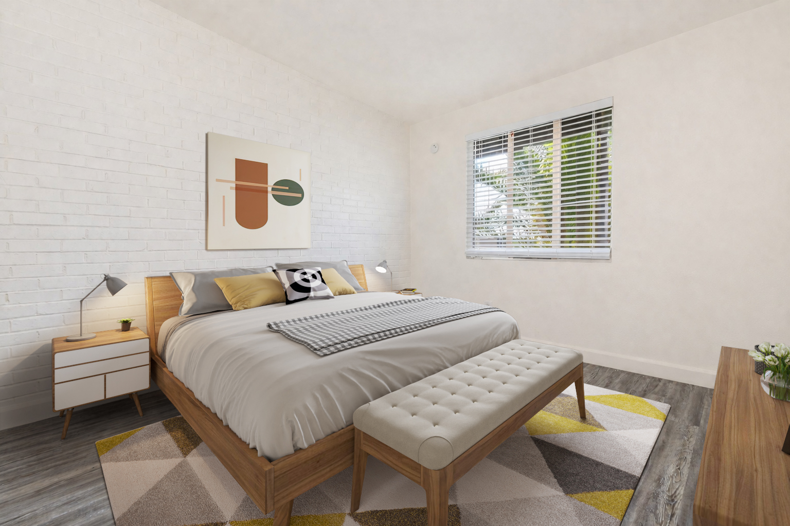 Modern bedroom featuring a large bed with gray bedding, decorative pillows, and a patterned throw. A tufted bench sits at the foot of the bed. The room has light-colored walls, a geometric rug, a stylish nightstand with a lamp, and a framed artwork on the wall. Natural light filters through a window with blinds.