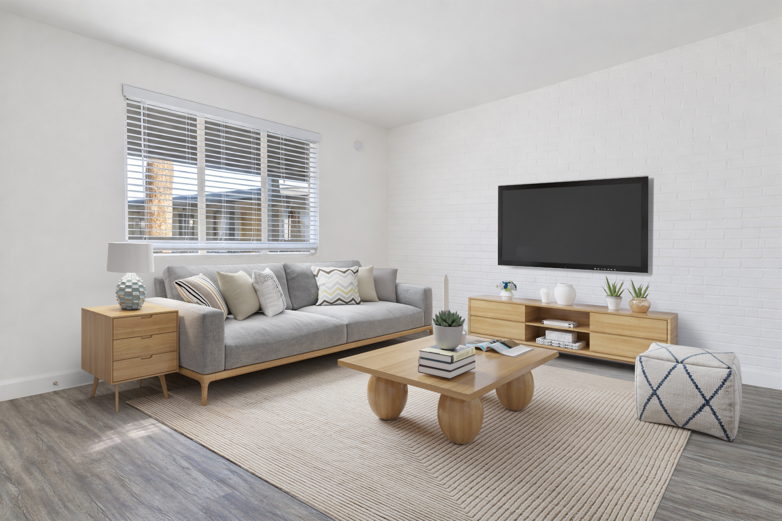 A modern living room featuring a light gray sofa with decorative pillows, a wooden coffee table, and a matching side table. A large flat-screen TV is mounted on a white brick wall. Natural light streams in through a window with blinds, and potted plants adorn the furniture, creating a cozy and inviting atmosphere.