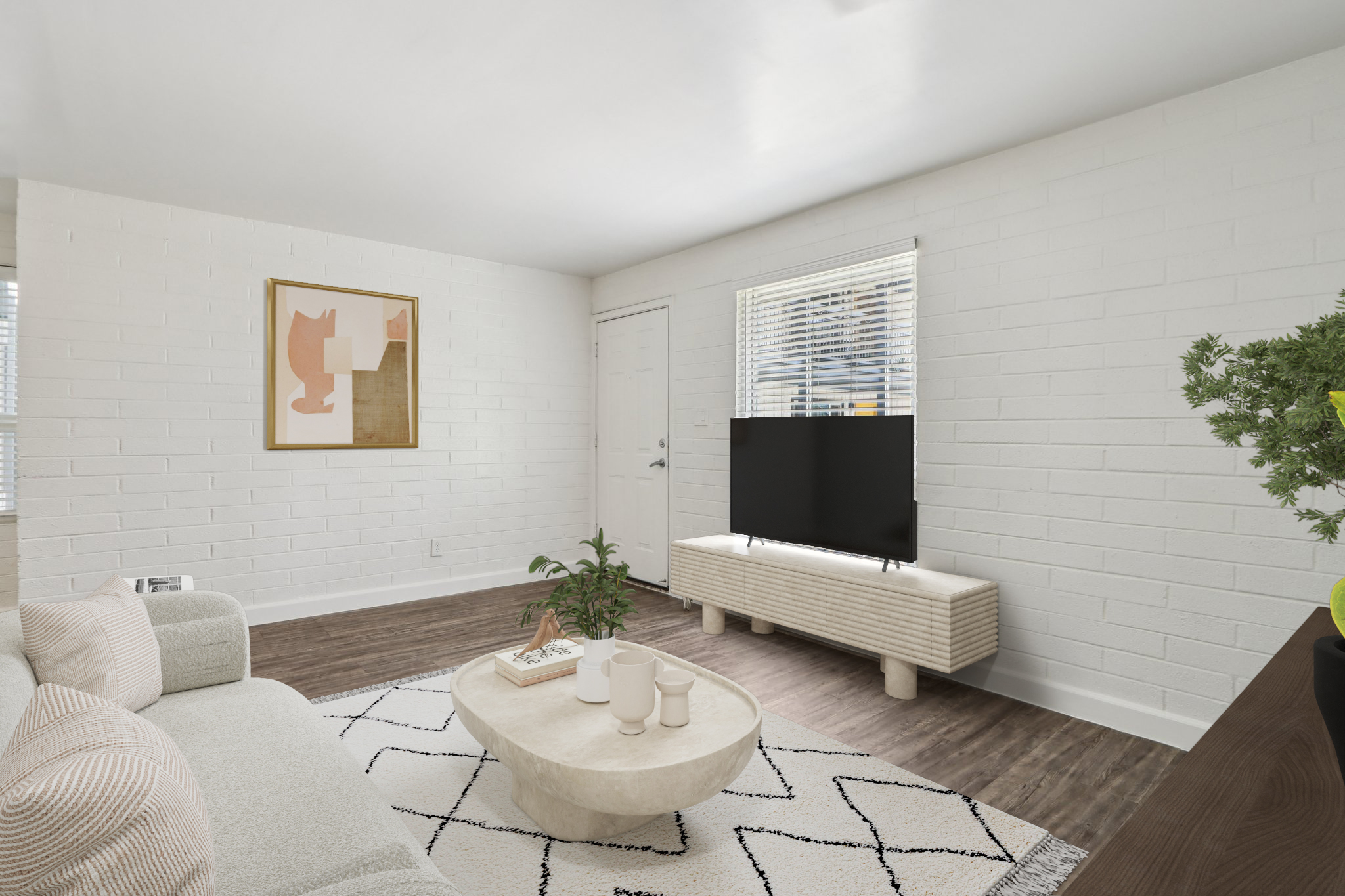 A bright and modern living room featuring a light-colored sofa with pink cushions, a round coffee table, and a television on a woven-style media console. The walls are white brick, and there is a plant and artwork on display, creating a cozy and stylish atmosphere. Natural light comes in through a window.