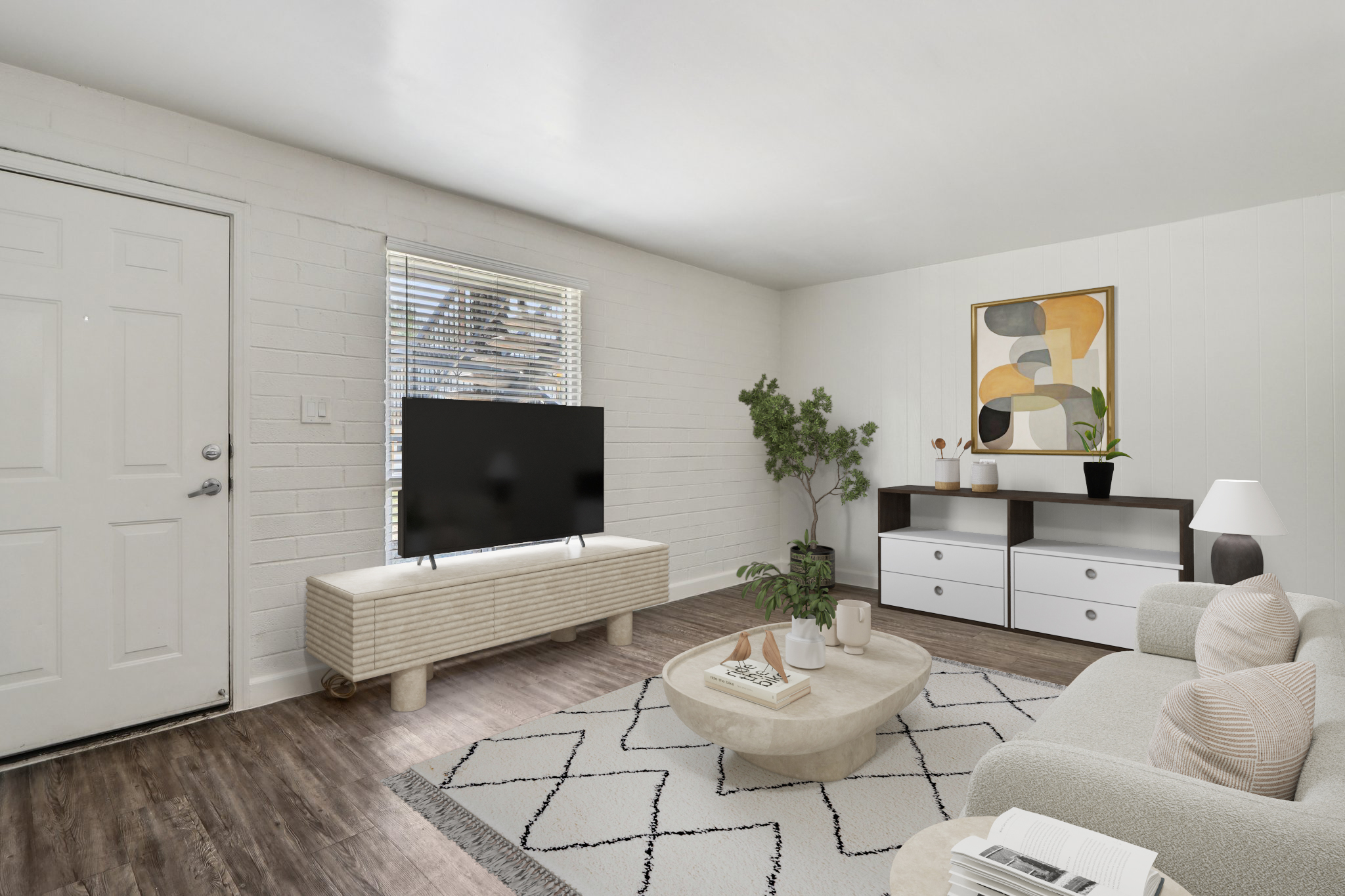 A bright and modern living room featuring a light-colored couch, a round coffee table, and a large flat-screen TV on a textured media console. A window allows natural light in, with a decorative plant in the corner. The walls are plain white, and there's a minimalist wall art piece nearby.
