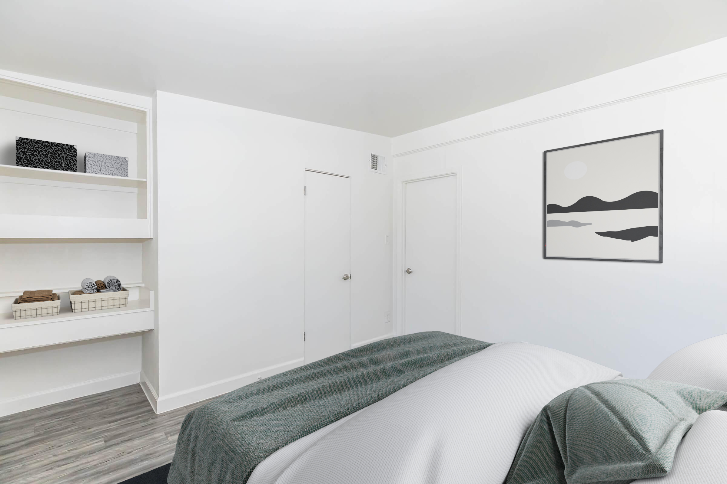 A modern bedroom featuring a cozy bed with a gray blanket and pillows, minimalist decor, and white walls. There's a shelf with neatly arranged towels and a framed abstract landscape artwork on the wall. The flooring is light-colored, enhancing the bright, airy atmosphere of the room.