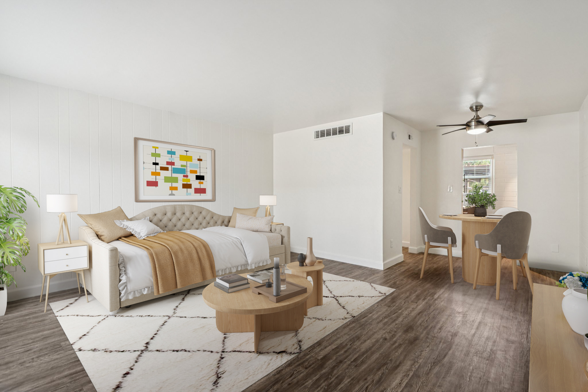 A modern, stylish bedroom with a beige tufted bed, light-colored bedding, and decorative pillows. A large piece of abstract art hangs on the wall. The room features a round coffee table with decor items, a dining area with a small table and chairs, and a floor lamp. Natural light streams in through a window, enhancing the bright ambiance.
