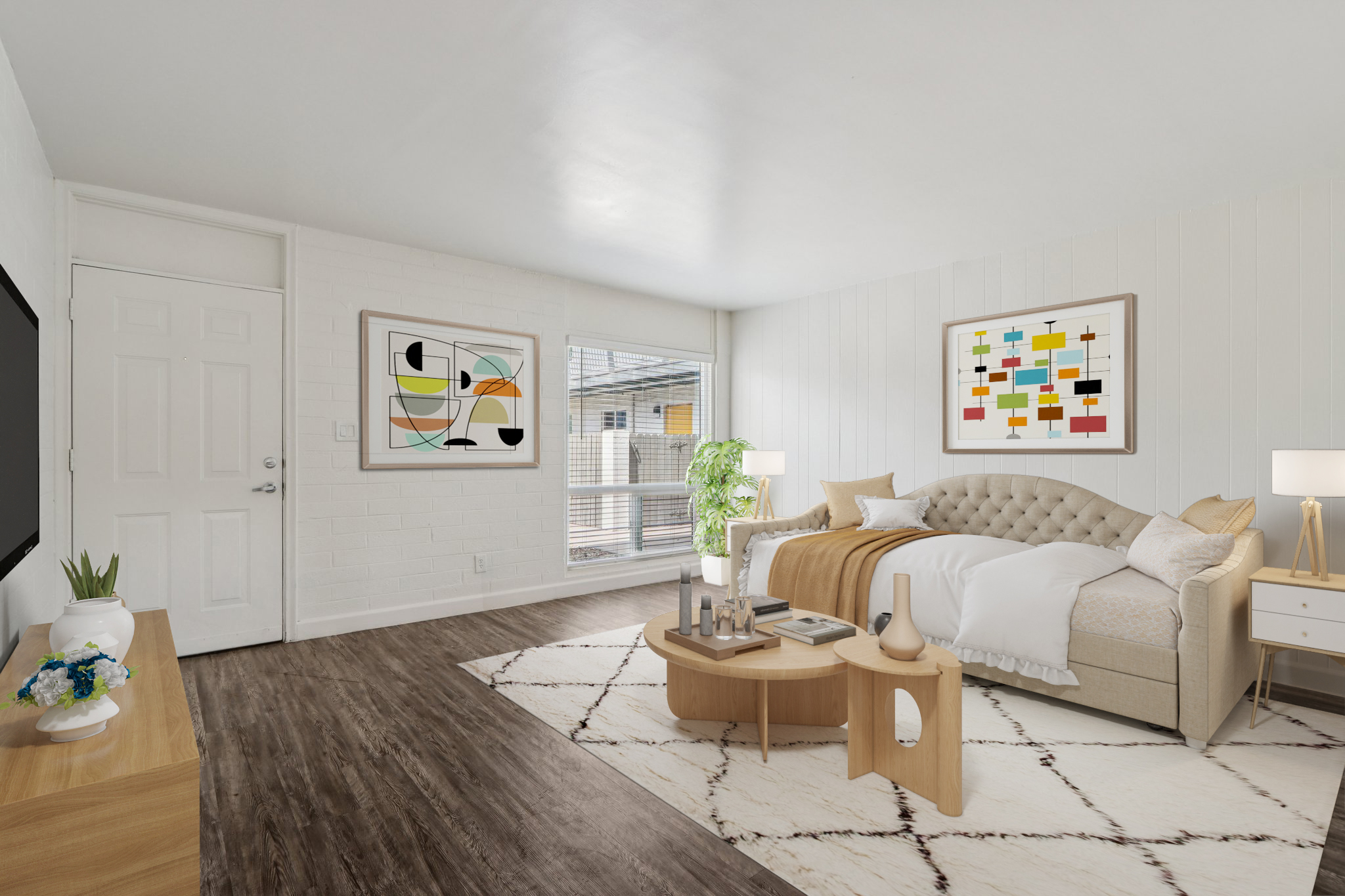 A cozy bedroom featuring a beige tufted bed with a decorative throw blanket, a round wooden coffee table, and a television against a white wall. Large windows provide natural light, with green plants and colorful abstract art enhancing the space. The flooring is dark wood, and a light rug adds warmth.