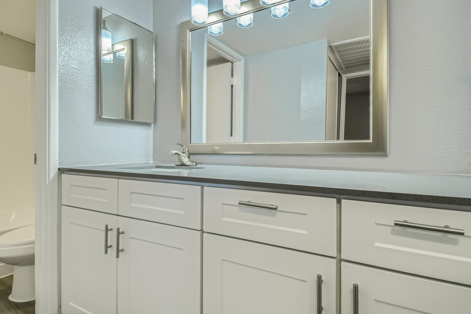 A bathroom with white cabinets and a mirror in an apartment at Rise North Ridge