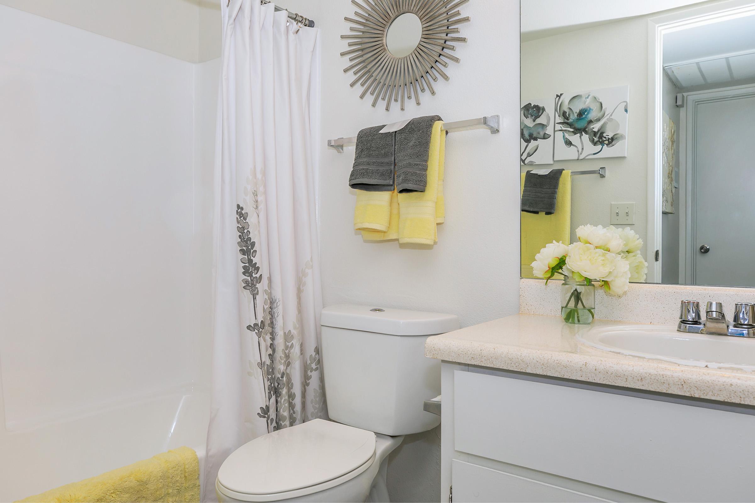 A bathroom with yellow towels, a white vanity and a shower at Rise North Ridge.