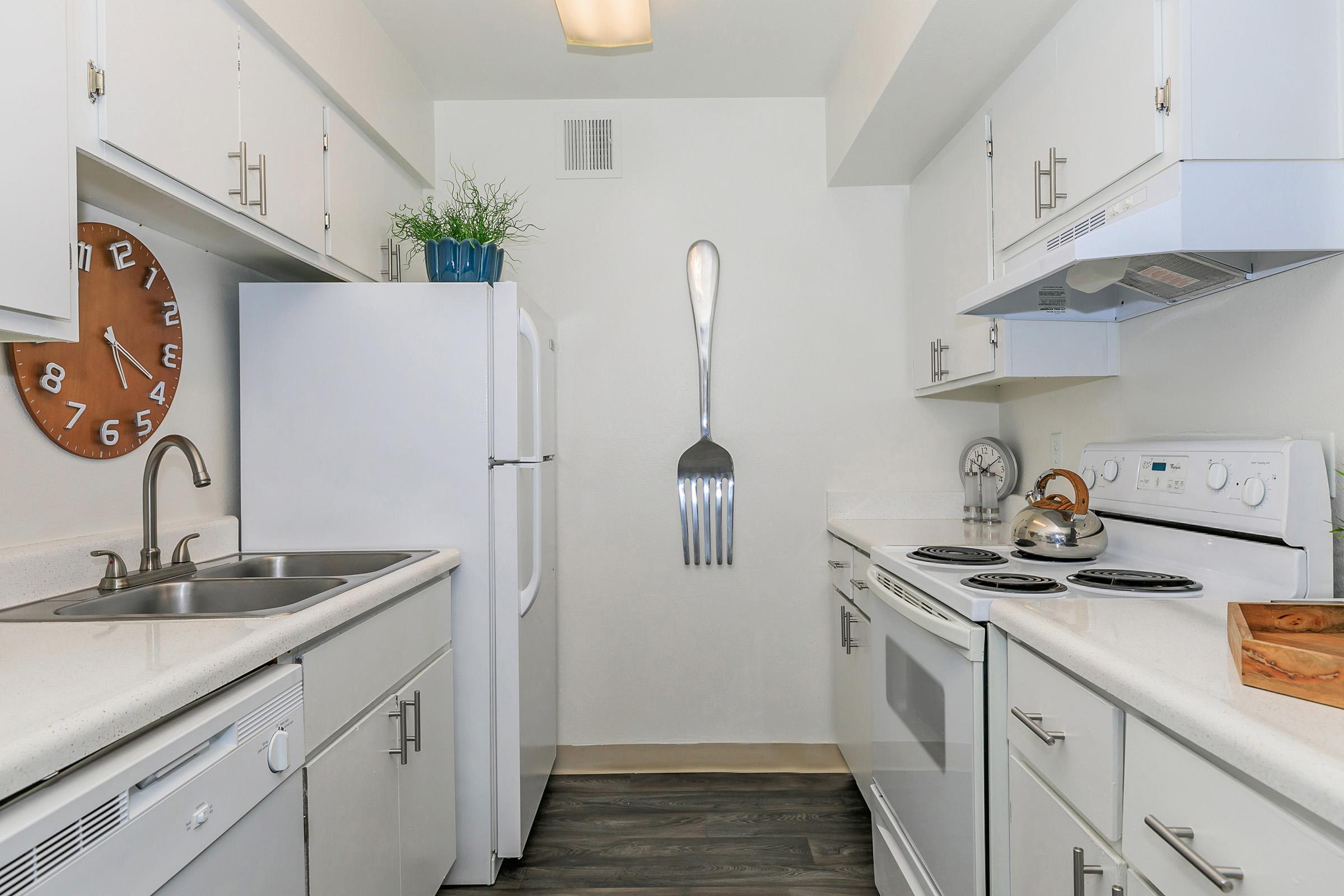 A galley kitchen with white cabinets and white appliances at Rise North Ridge.