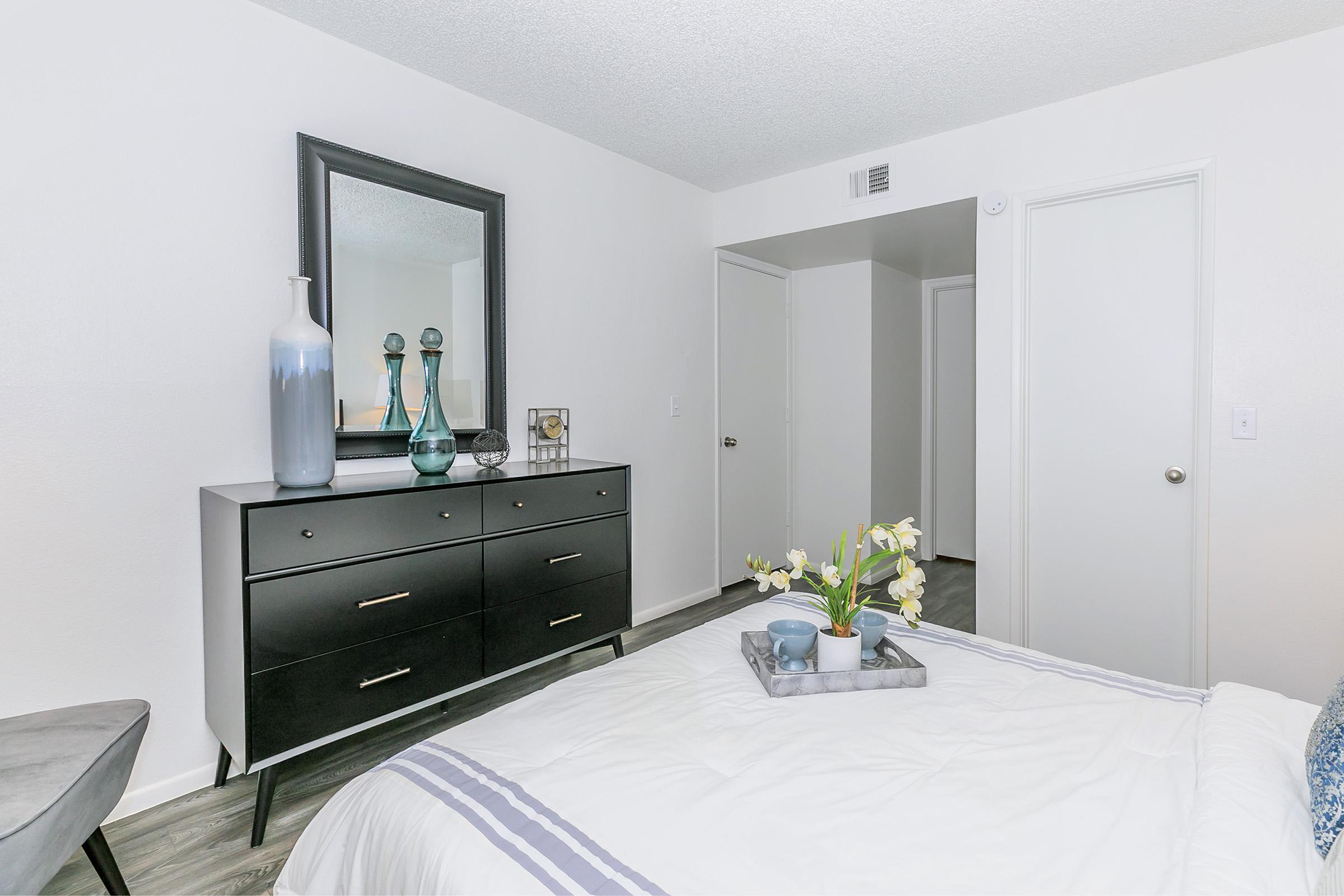 An apartment bedroom with a queen bed and a dresser at Rise North Ridge.