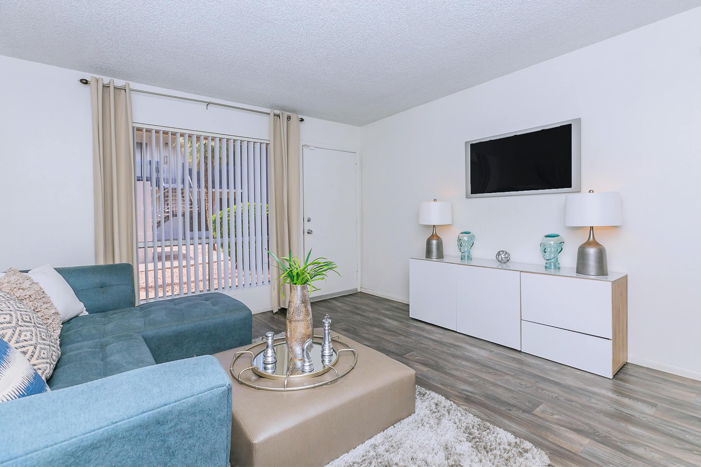 An apartment with a blue couch, wood-style floors, and sliding doors to a patio at Rise North Ridge.