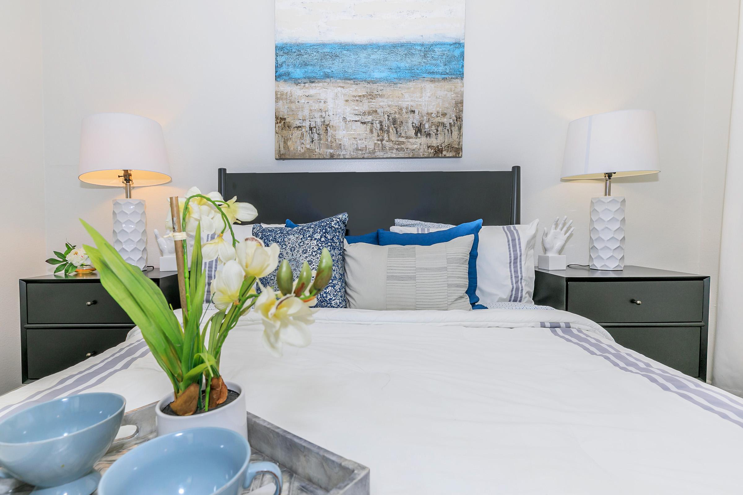 Close up view of a large bed, 2 night stands, wall art, and a breakfast tray in a bedroom at Rise North Ridge.