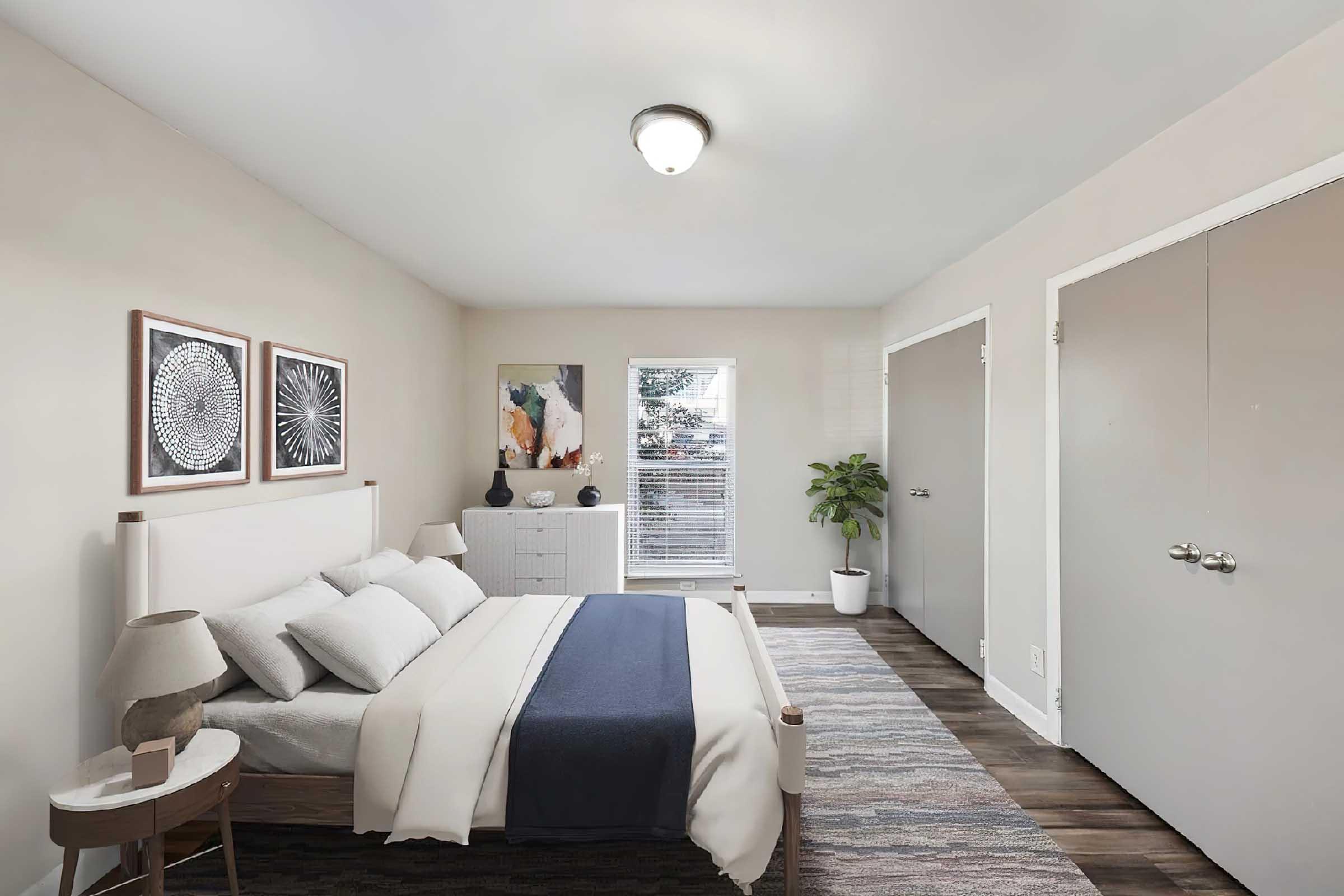 A cozy bedroom featuring a bed with white linens and a blue throw blanket. There are framed artworks on the wall, a white dresser, a bedside table with a lamp, and a potted plant. Natural light comes through a window, enhancing the warm and inviting atmosphere of the space.