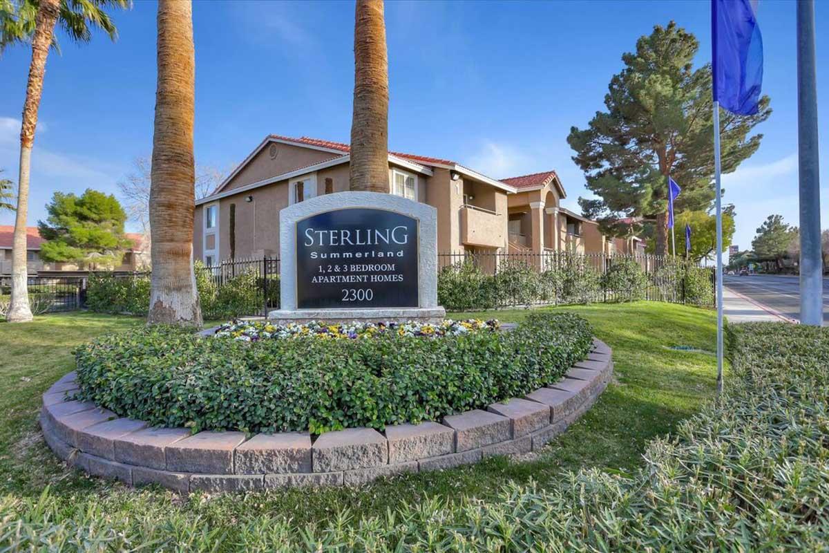 Sign for Sterling Summerland Apartments located at 2300, showcasing a landscaped area with palm trees and decorative bushes. The building in the background features a modern architectural style, and clear blue skies enhance the inviting atmosphere of the property.