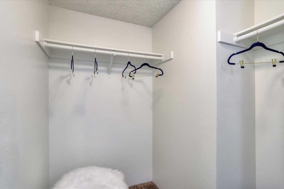 Empty closet space with white walls and a single shelf. Several hangers are hanging from a rod, and there's a fluffy white item on the floor. The space appears clean and organized, suitable for storage or clothing.