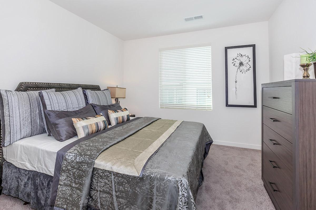 Four-Bedroom Townhomes in Chula Vista, CA - Contessa at Otay Ranch - A Bedroom with Soft Carpet Flooring, a Wooden Dresser, and a Window.