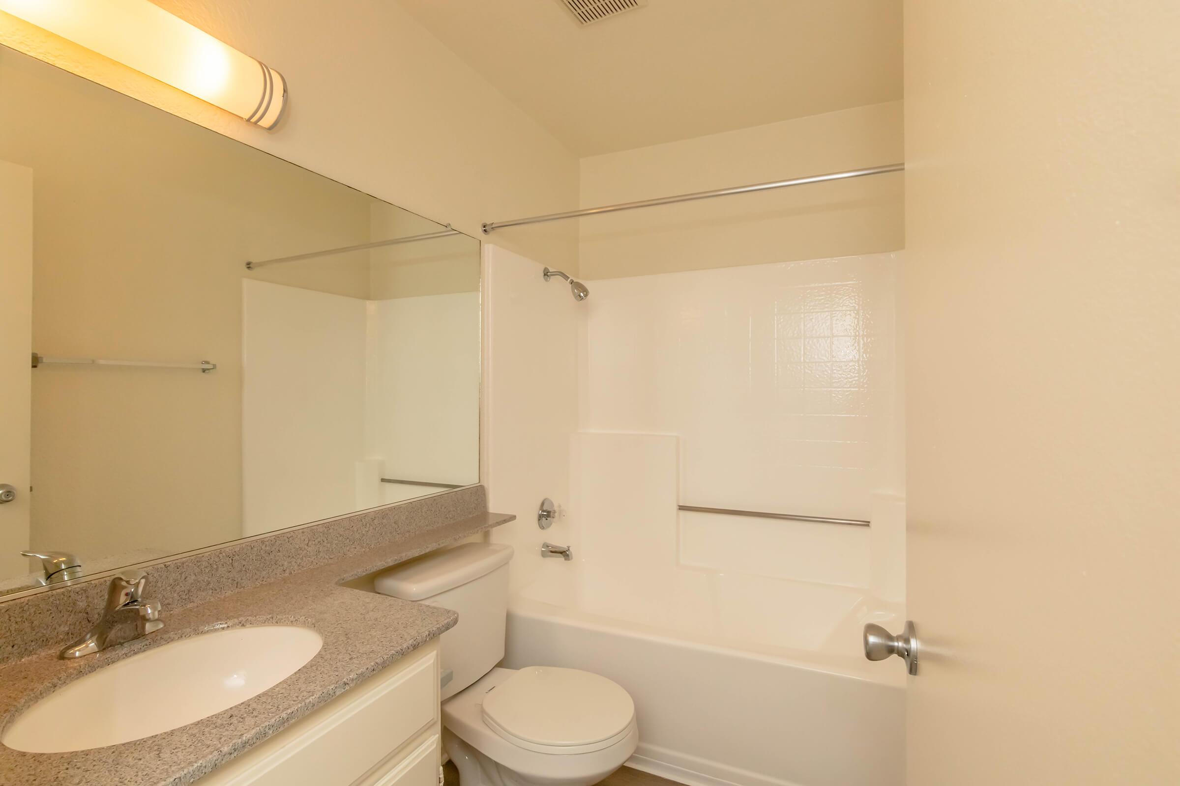A clean, well-lit bathroom with a bathtub, shower, and toilet. The vanity features a sink with a mirror above it. The color scheme is neutral, and there is a towel rack on the wall. The overall appearance is simple and functional, suitable for daily use.