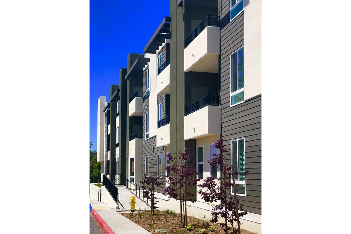 Modern apartment building featuring multiple stories with balconies, large windows, and a mix of light and dark exterior finishes.