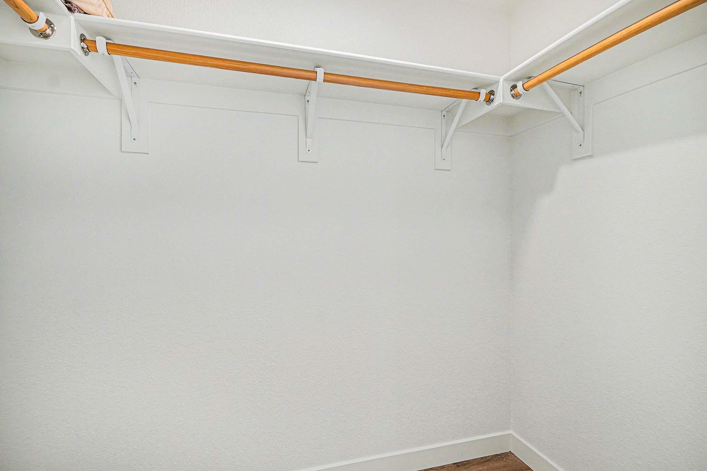 A clean, empty closet featuring white walls and two parallel clothing rods with wooden accents. The floor is wooden, and there's a sense of spaciousness, with no items or decorations present in the space.