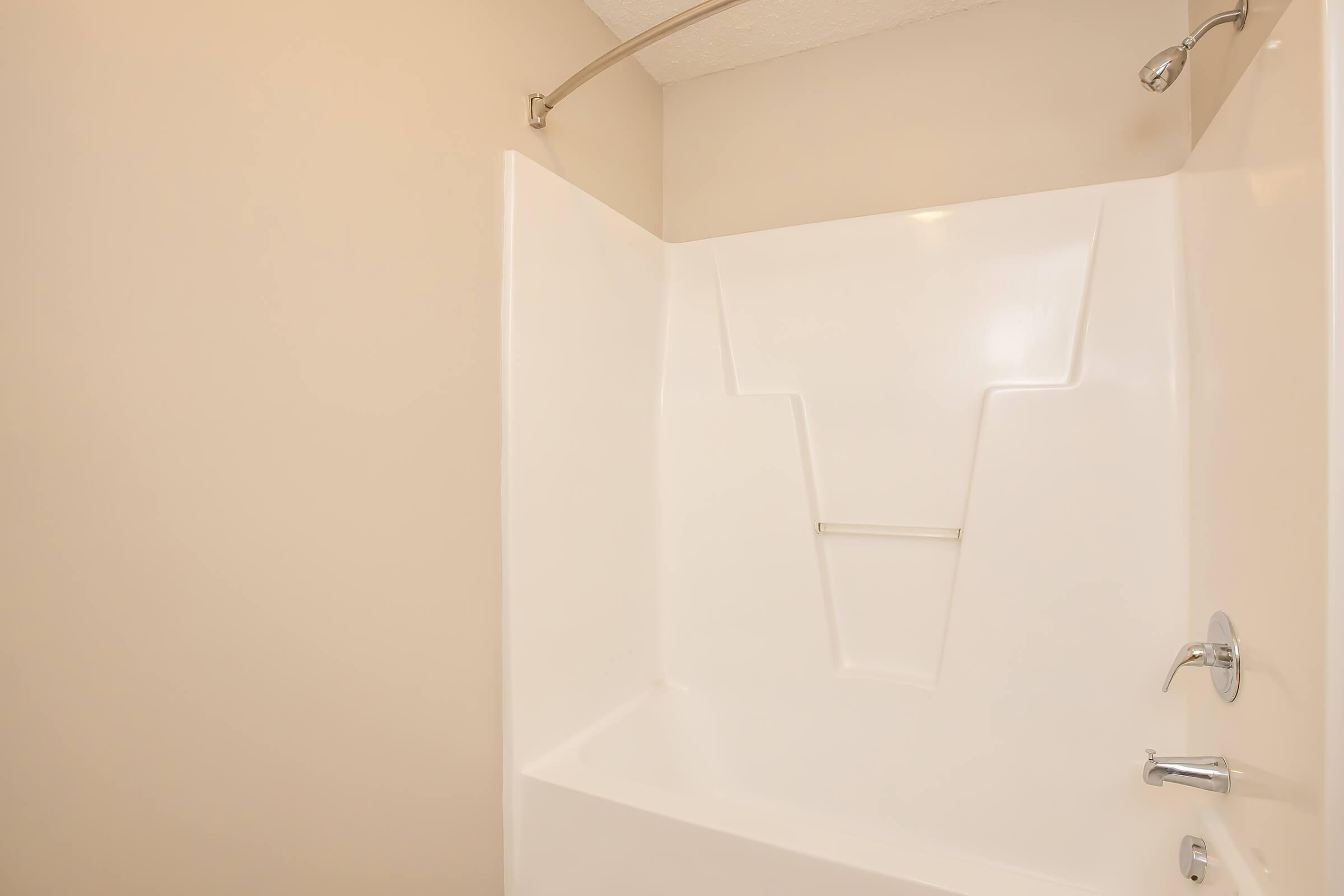 A clean and empty bathroom shower stall with a white, smooth fiberglass interior. The design features a simple, modern appearance with a chrome showerhead and faucet. The walls are painted a neutral beige color, providing a bright and airy feel to the space.