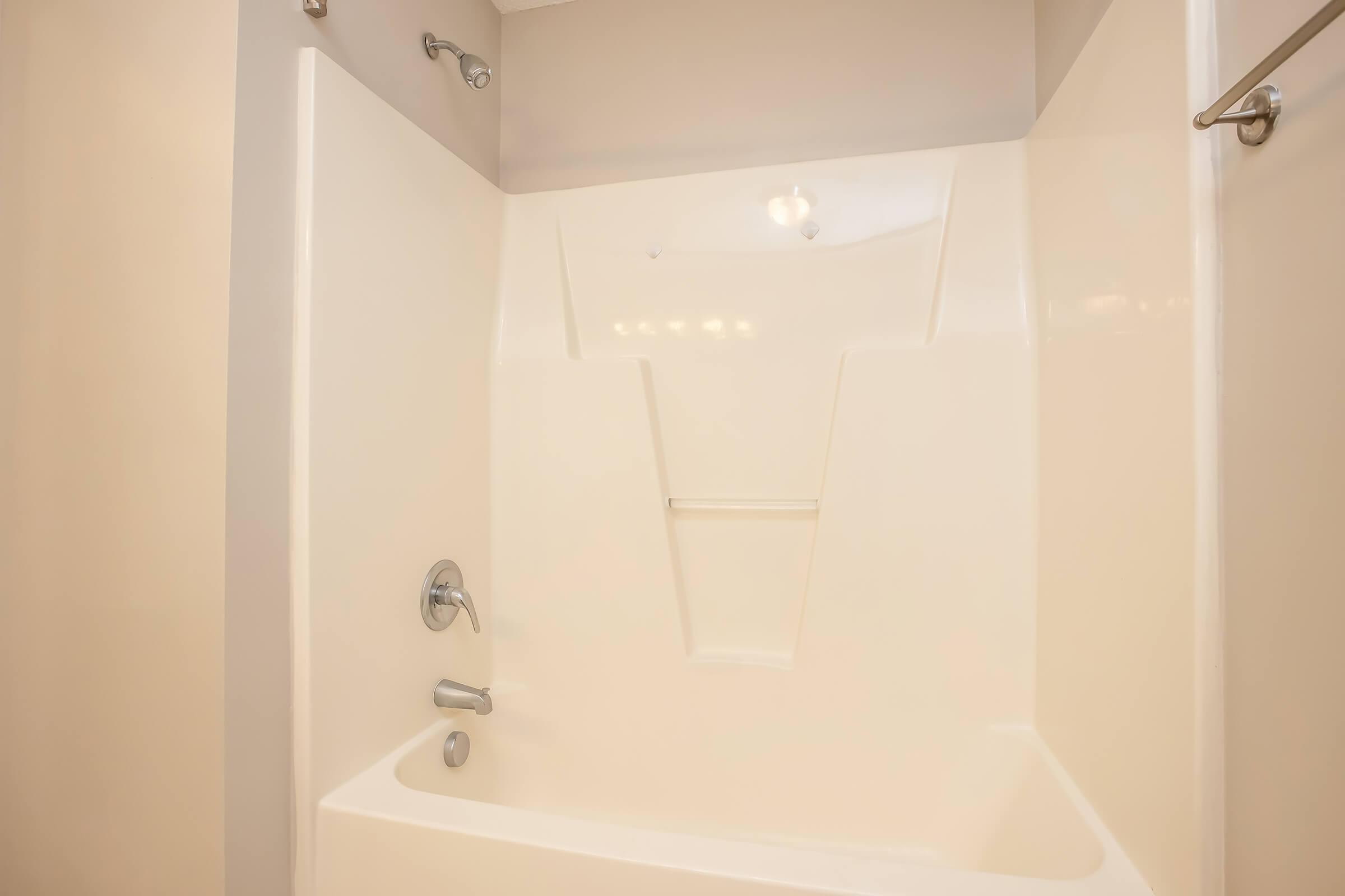 A clean and empty shower stall with white walls and a built-in bench. The fixtures, including a showerhead and faucet, are metal and modern. The space is well-lit and minimalistic, creating a bright and airy atmosphere.