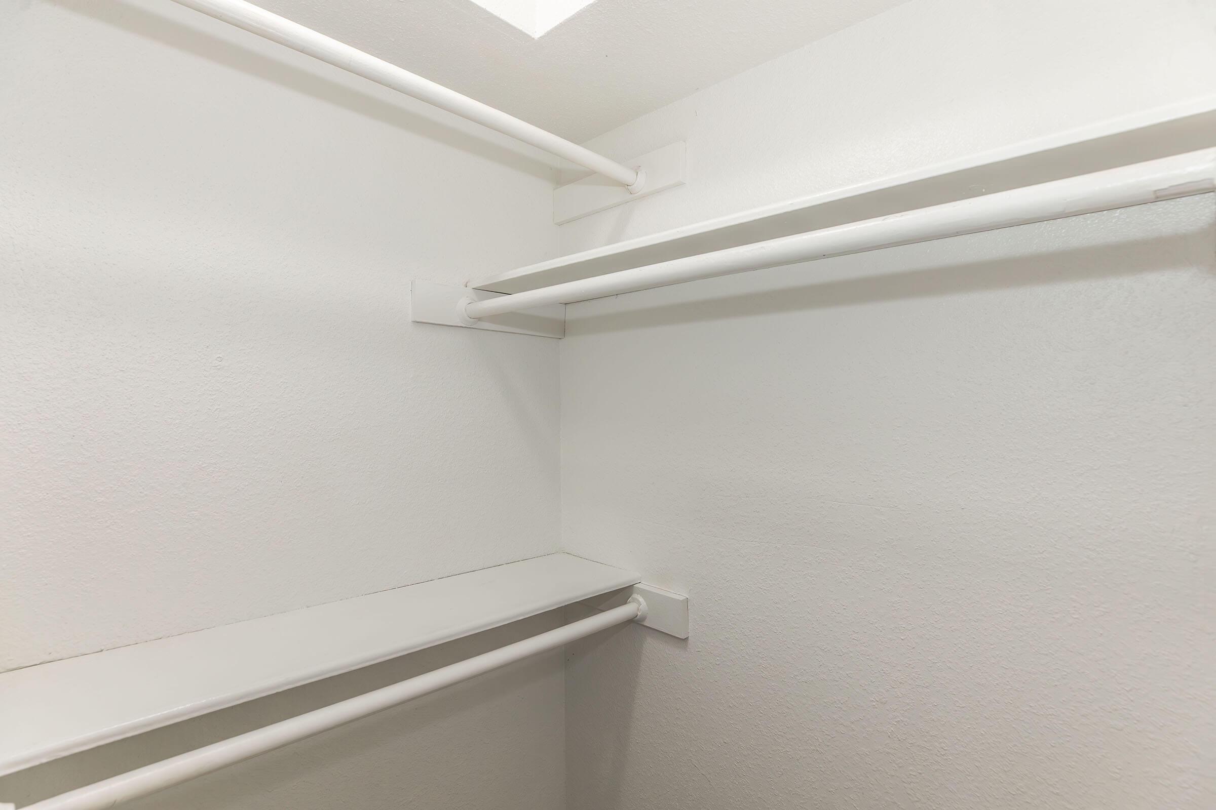 A clean and empty closet featuring white walls and two horizontal clothing rods, with one shelf located above. The interior is well-lit and organized, showcasing a minimalist design.