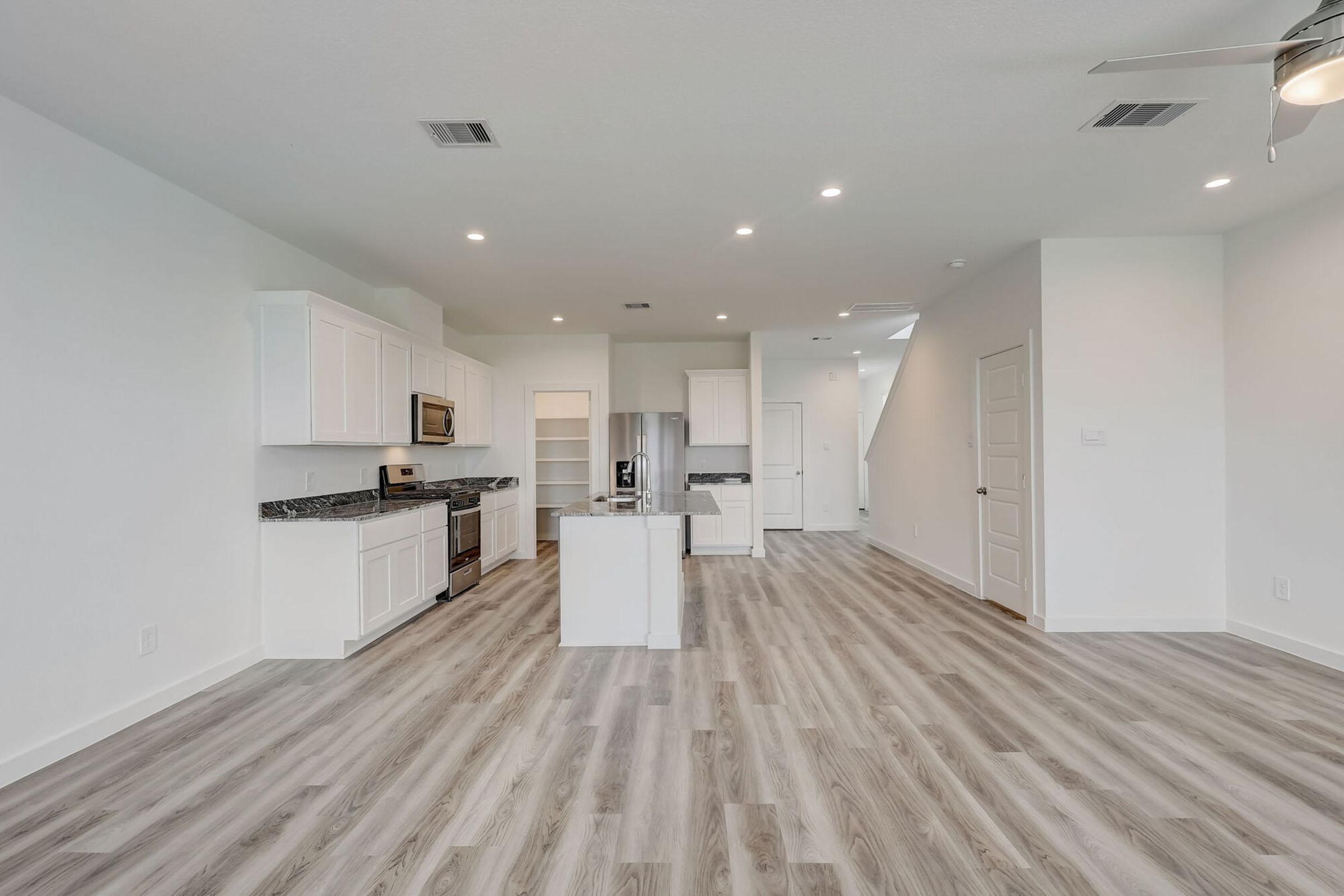Modern open-concept kitchen and living area featuring white cabinets, stainless steel appliances, and a center island. The space has light hardwood flooring and recessed lighting, creating a bright and airy atmosphere. Neutral walls enhance the contemporary design of the room.