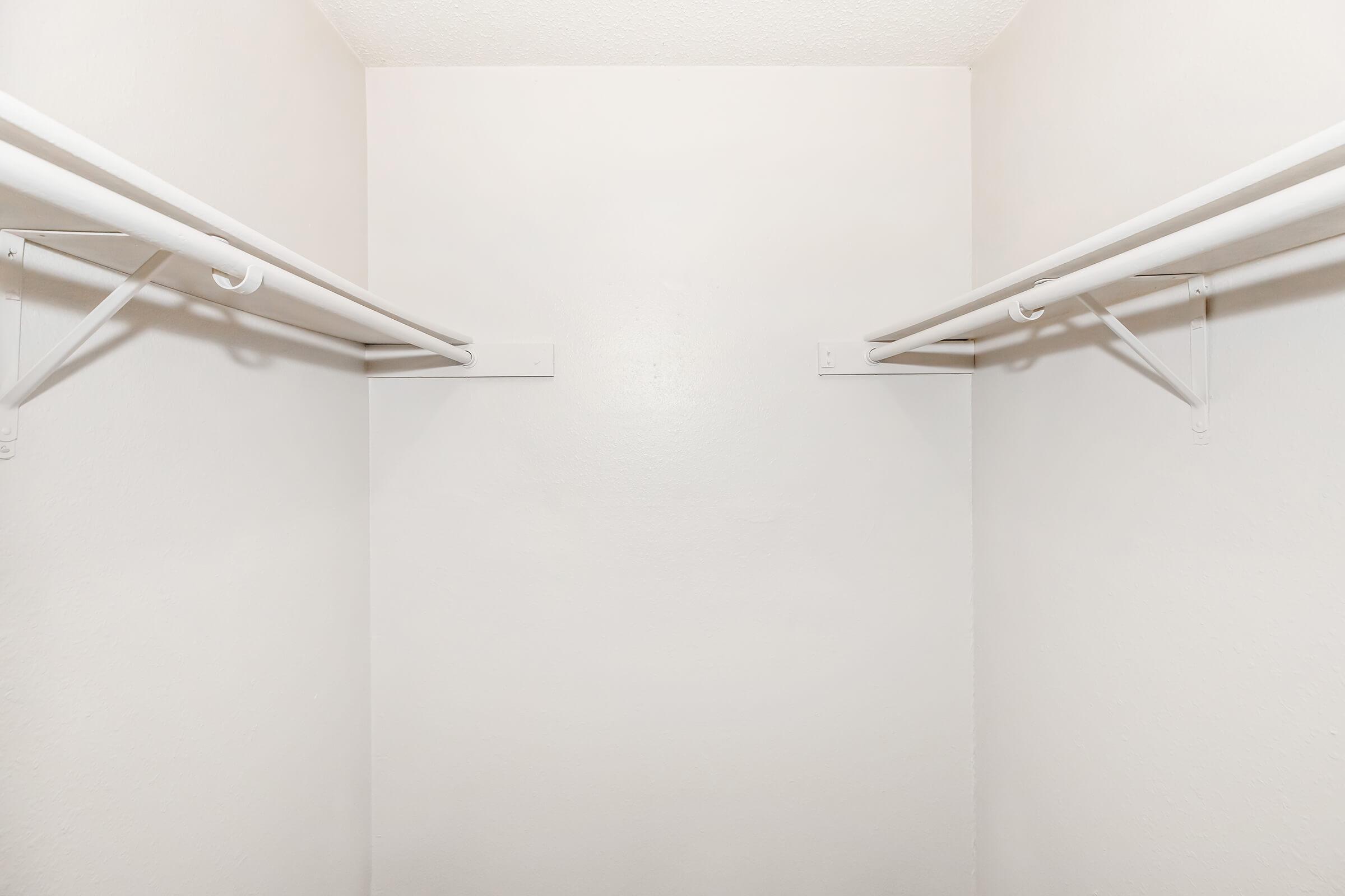 Empty closet with white walls and two hanging rods. The minimalistic space has no shelves or items present, creating a clean and simple look.