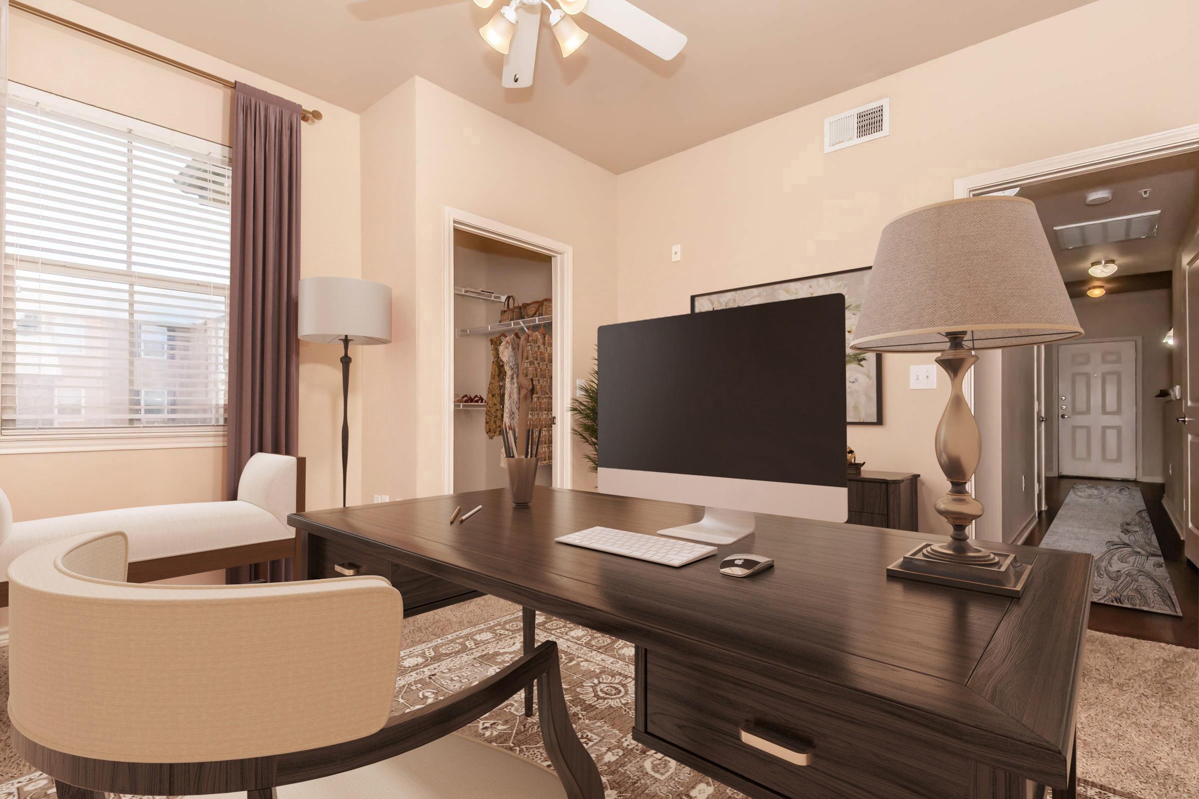 A modern office space featuring a sleek desk with a computer and a lamp, surrounded by a comfortable chair and an armchair. There's a window with sheer curtains allowing natural light, and a hallway is visible in the background, leading to an open door. The decor is warm and inviting.