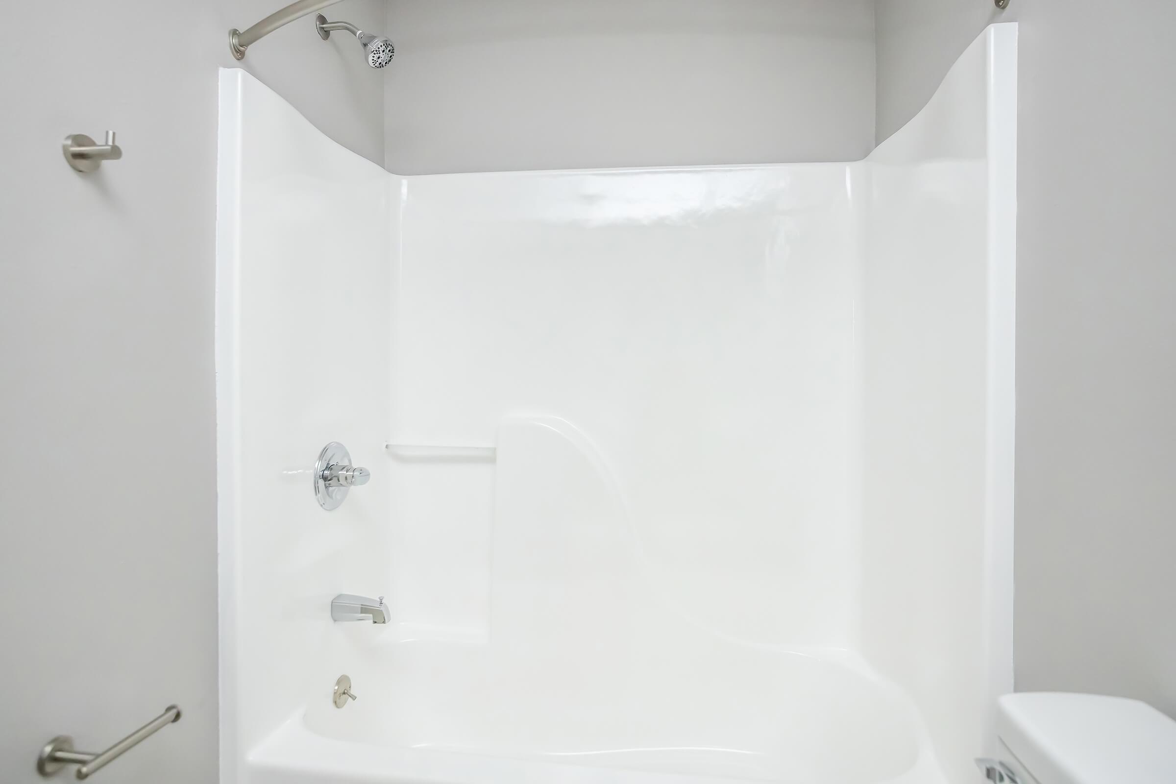 A clean, modern bathroom with a white shower stall featuring a grab bar, a showerhead attached to the wall, and a sleek tub design. The walls are light-colored, contributing to a bright and airy atmosphere. The space is uncluttered, emphasizing a minimalist aesthetic.