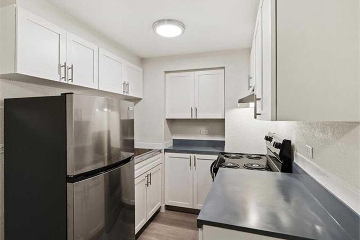 Modern kitchen with white cabinetry, a stainless steel refrigerator, and a black stove. The countertops are dark, and there is an overhead light. The walls are light-colored, providing a bright and clean look.