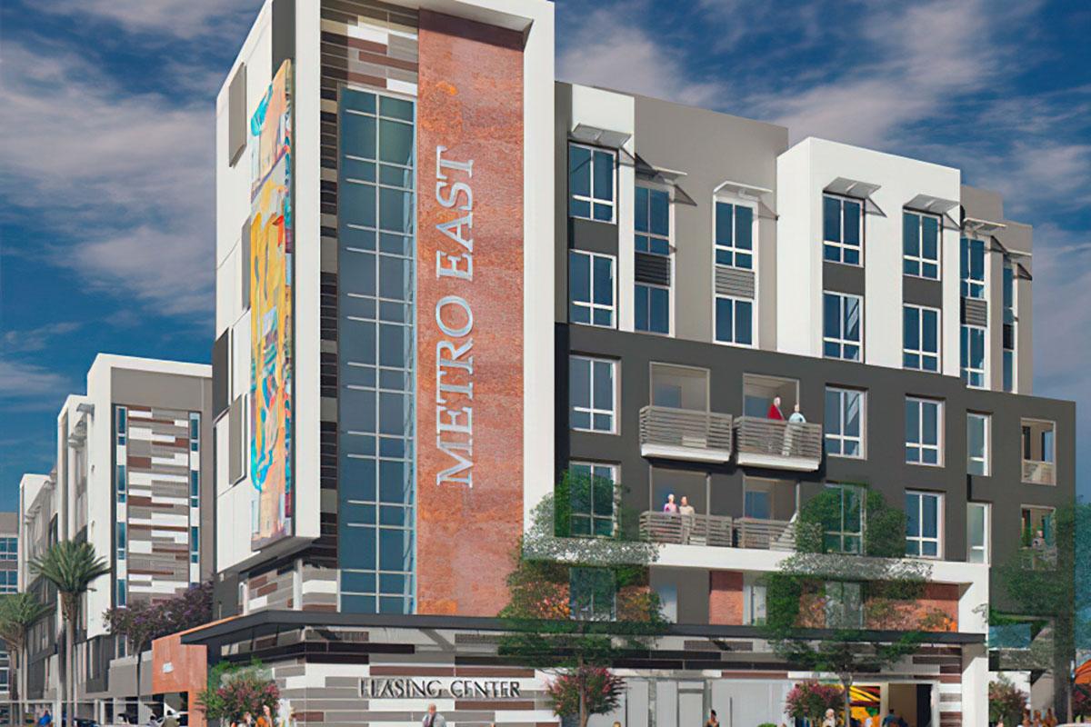 Rendering of a modern multi-story residential building named "Metro East." The facade features a mix of brick and contemporary design elements, with balconies visible on several floors.