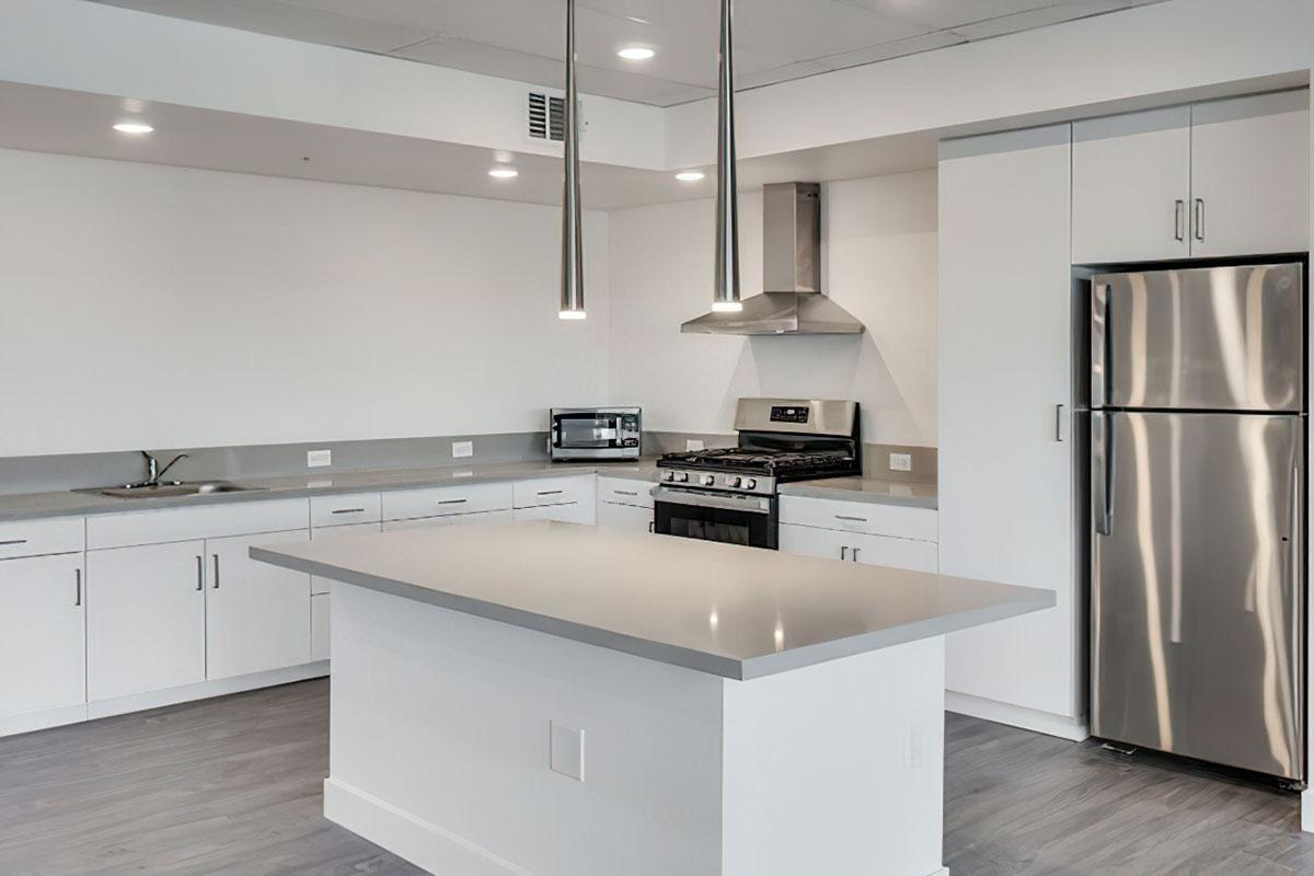Modern kitchen featuring a central island, sleek white cabinets, stainless steel appliances including a refrigerator and gas stove, and stylish pendant lighting.