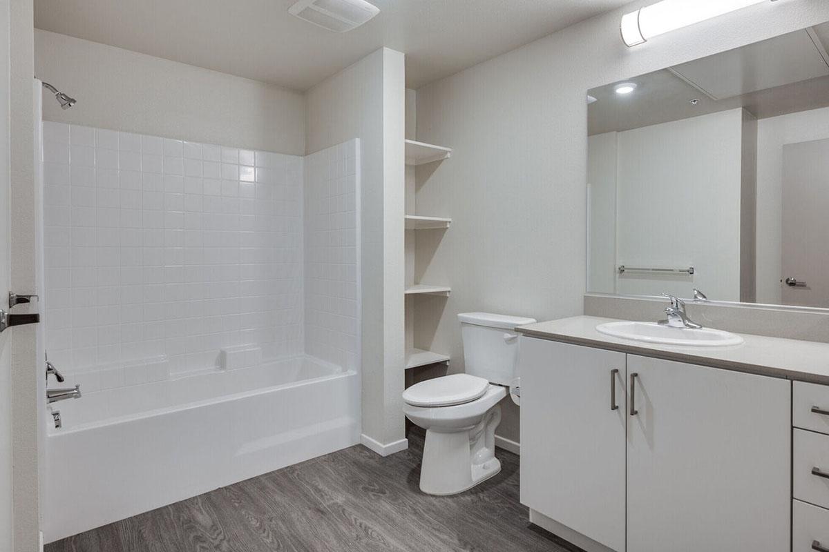 A clean, modern bathroom featuring a white bathtub with a shower, a white toilet, and a sink with a countertop.