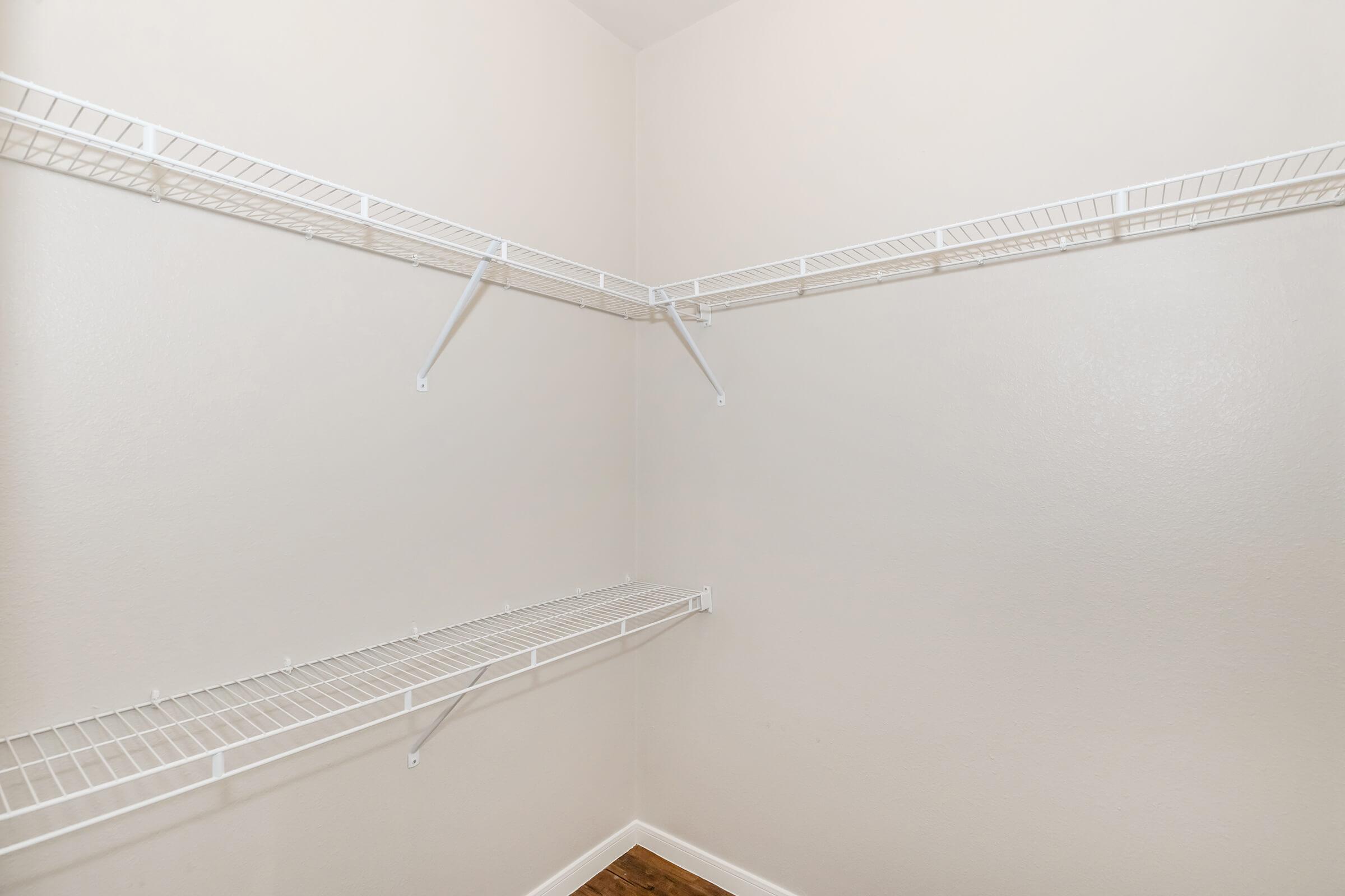 Empty closet corner with white wire shelves mounted on beige walls. The floor is wooden, and the space is well-lit, providing a clean and organized feel.