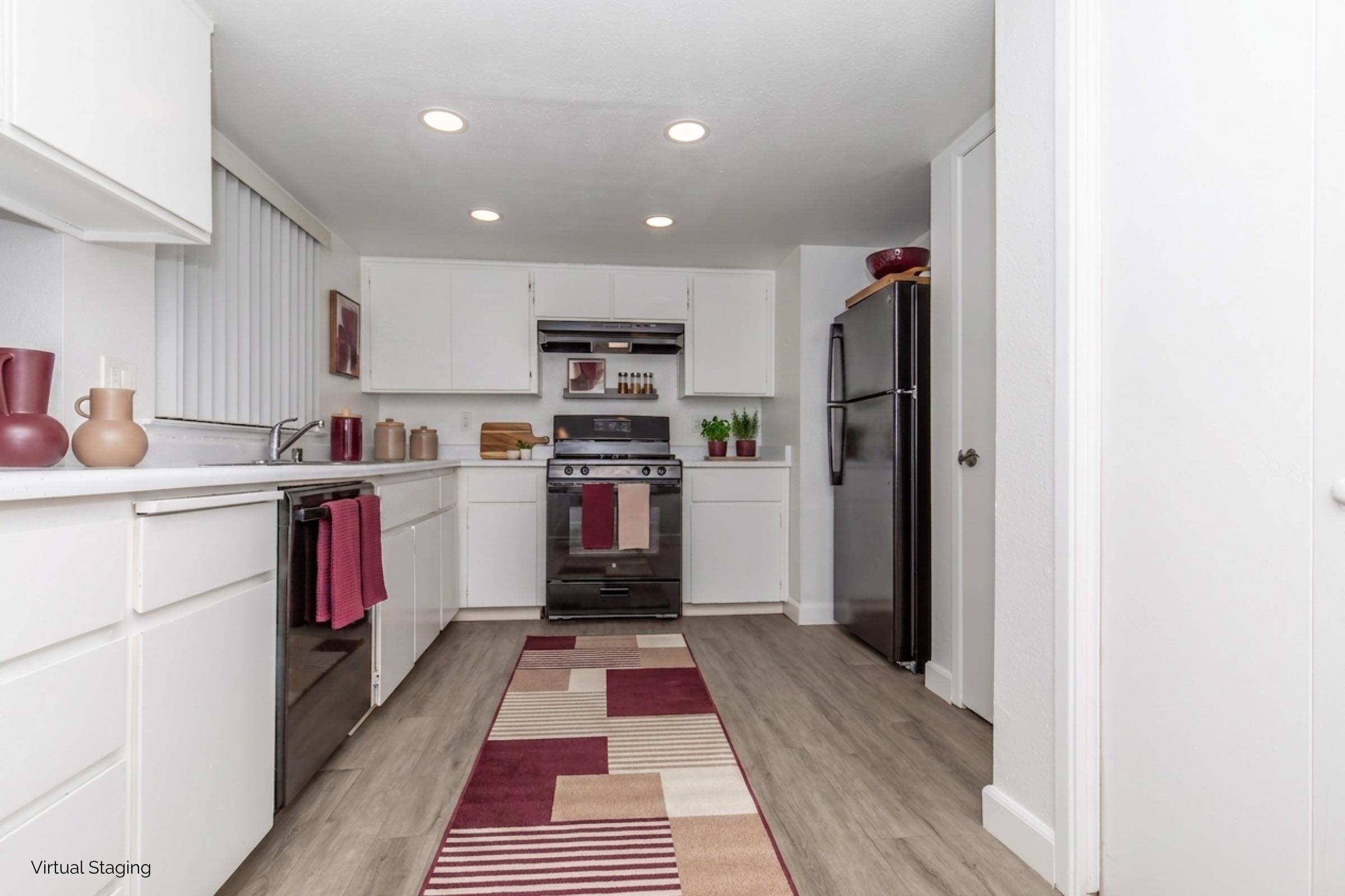 A modern kitchen featuring white cabinets, stainless steel appliances, and a black refrigerator. There is a colorful rug on the floor with geometric patterns. The countertop has decorative items, including vases and kitchen utensils. Bright lighting enhances the open and clean space.