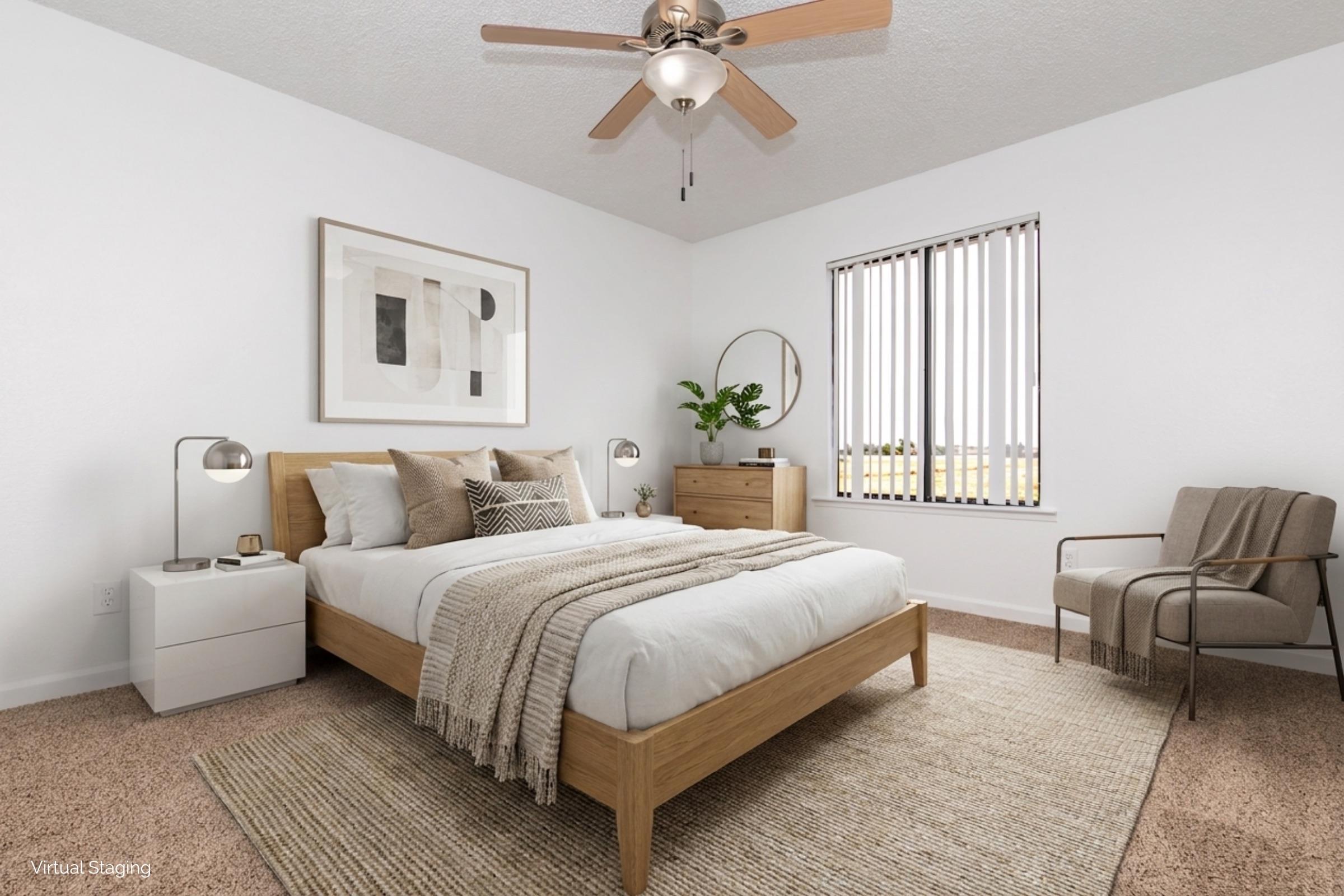 A modern bedroom featuring a wooden bed with white bedding and decorative throw pillows. There’s a nightstand with a lamp, a cozy armchair, and a dresser. Large windows with vertical blinds let in natural light, and a round mirror and framed artwork decorate the walls. A textured rug adds warmth to the space.