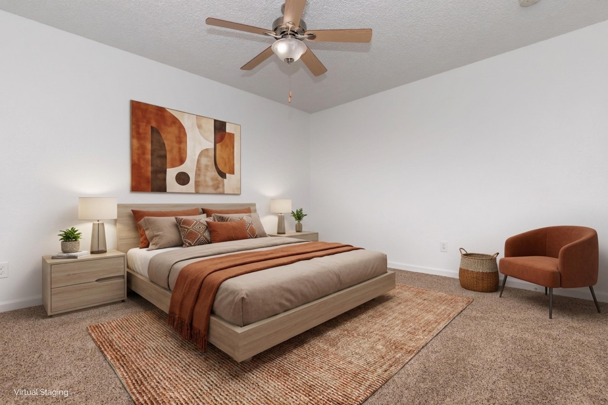 A cozy bedroom featuring a queen-sized bed with neutral-toned bedding and decorative pillows. There are two bedside lamps on either side, a modern artwork piece on the wall, and a stylish brown chair next to a woven basket. The room has a soft carpet and a ceiling fan, creating a warm and inviting atmosphere.