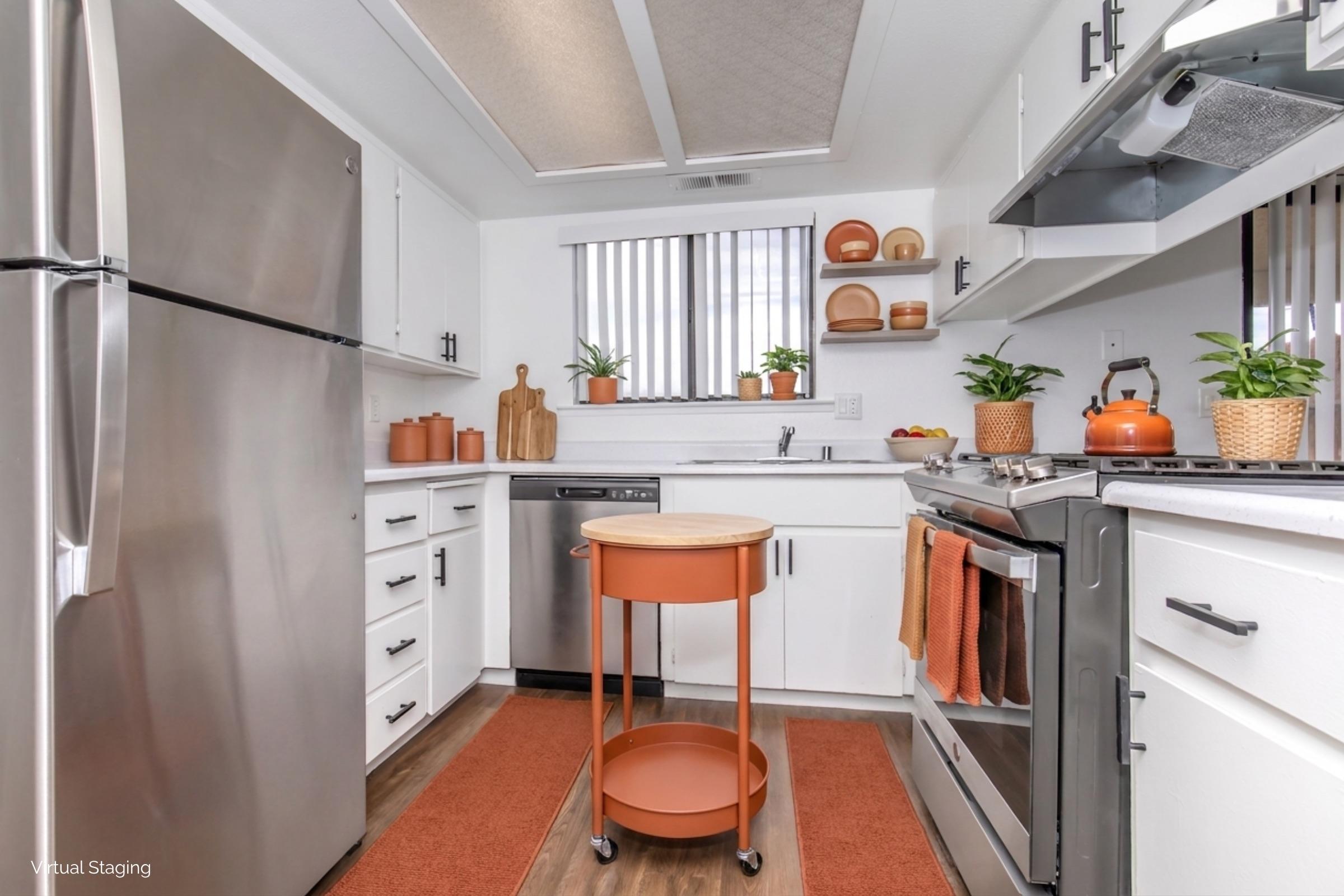 Modern kitchen featuring stainless steel appliances, including a refrigerator and dishwasher. The space is designed with white cabinets, wooden accents, and orange decor. A small round cart sits in the center, surrounded by potted plants and bowls. The floor is covered with a cozy area rug.
