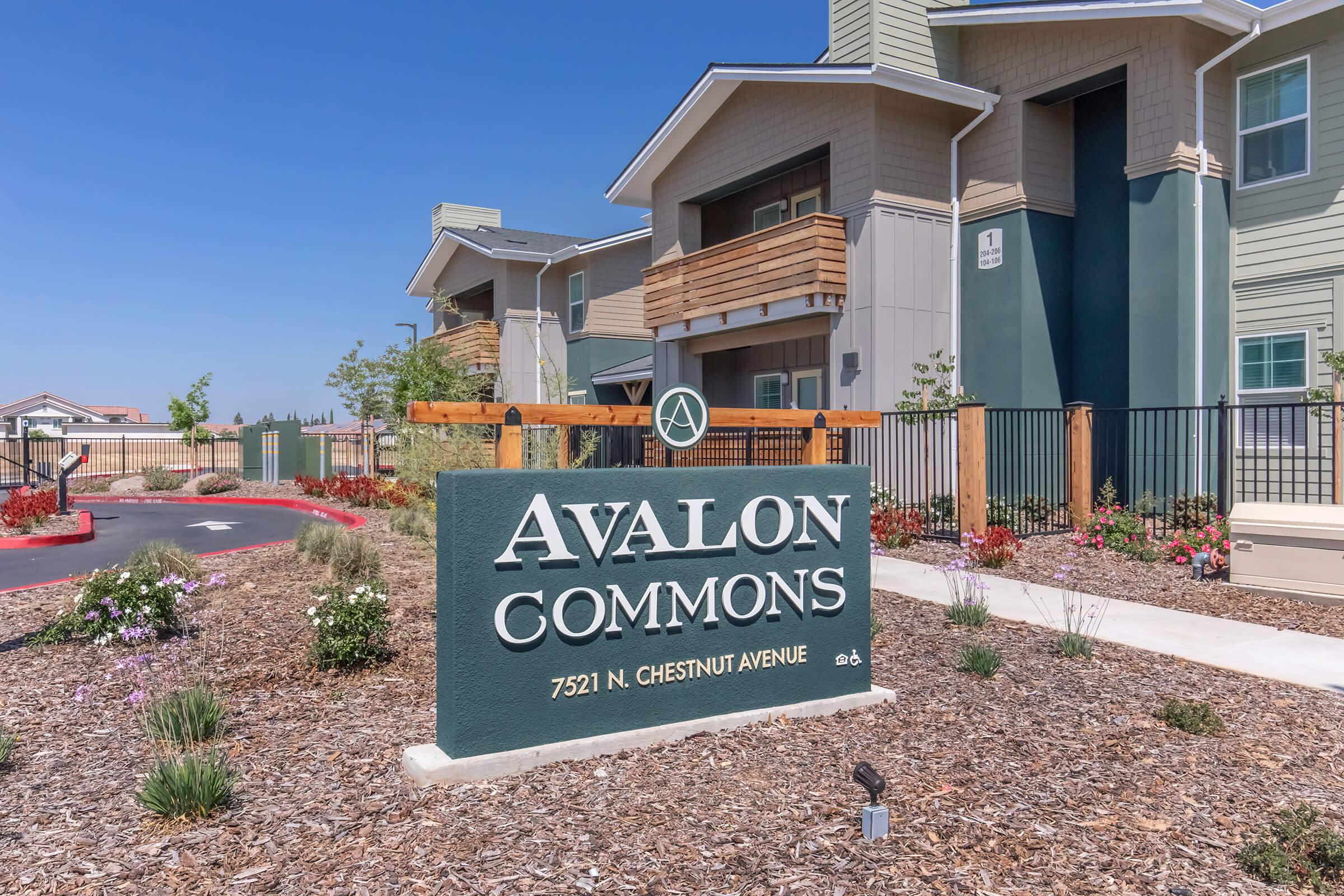 Sign for Avalon Commons, featuring the name prominently displayed. Surrounding landscaping includes flowers and shrubs, with buildings visible in the background. The scene is bright and well-maintained, indicating a residential area. Address listed as 7521 N. Chestnut Avenue.