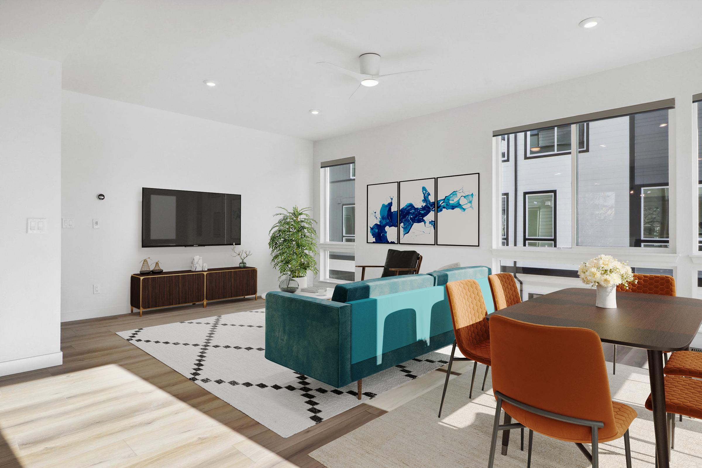 A modern living room featuring a teal couch, a wooden TV stand, and a dining area with orange chairs. Large windows provide natural light. Artwork with blue abstract designs is displayed on the wall. A potted plant and a vase of flowers add a touch of greenery and decor to the space.