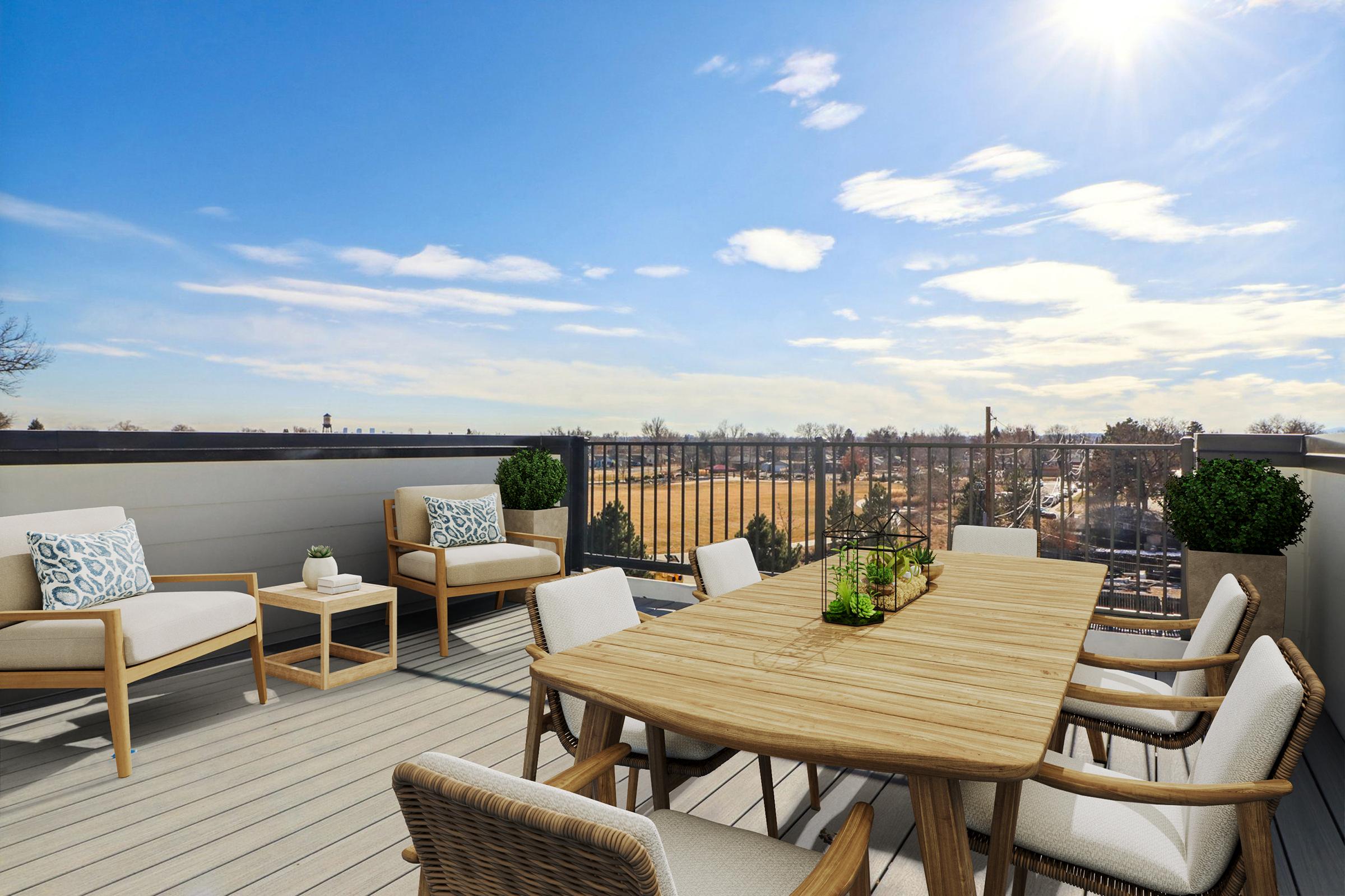 A spacious rooftop terrace featuring a wooden dining table surrounded by stylish chairs, complemented by comfortable seating areas. The scene includes potted plants and a clear blue sky, with sunlight shining brightly, creating a warm and inviting atmosphere.