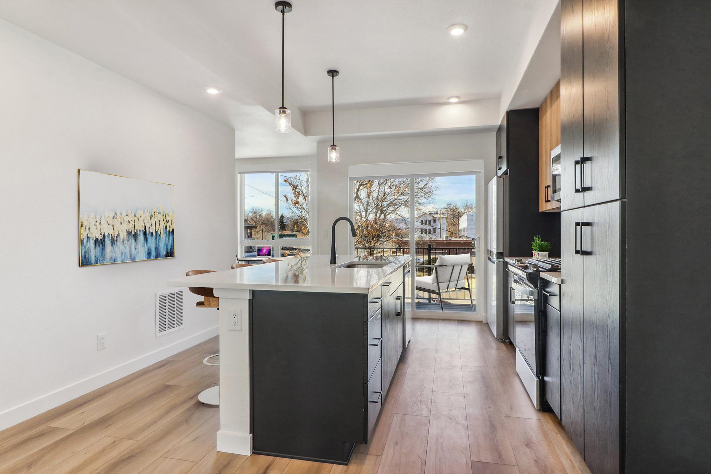 Modern kitchen featuring sleek cabinetry, a large central island with seating, and large windows that provide natural light. The space is decorated in neutral tones with a floral artwork on the wall, showcasing a contemporary design and an outdoor view from the adjacent balcony.