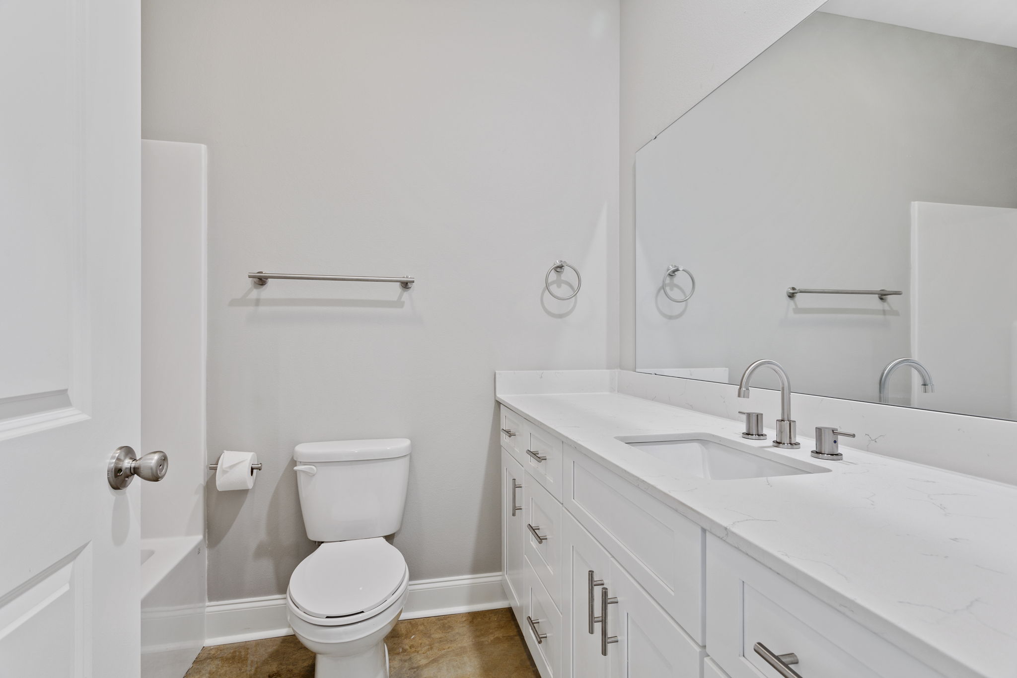 A modern bathroom featuring a white toilet, a sleek vanity with a sink, and a large mirror. The walls are painted in a neutral color, and there are towel bars and a toilet paper holder. The flooring is a light-colored tile, contributing to a clean and minimalistic design.