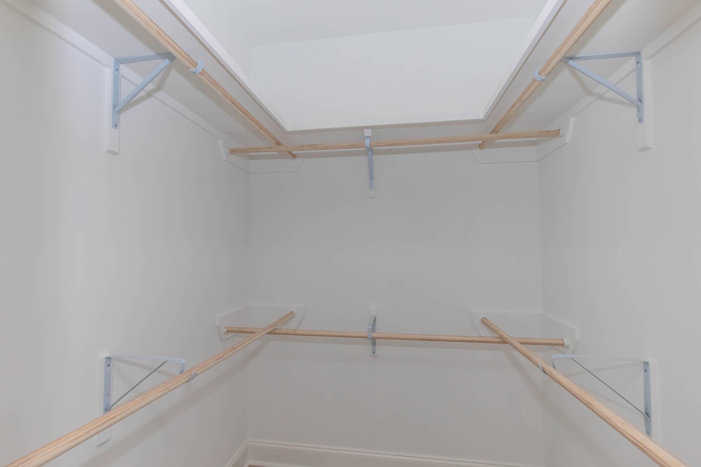 Empty closet with light-colored walls and wooden poles for hanging clothes, supported by metal brackets. The space has a clean and minimalist design, with no items or shelves present, emphasizing a tidy and organized appearance.