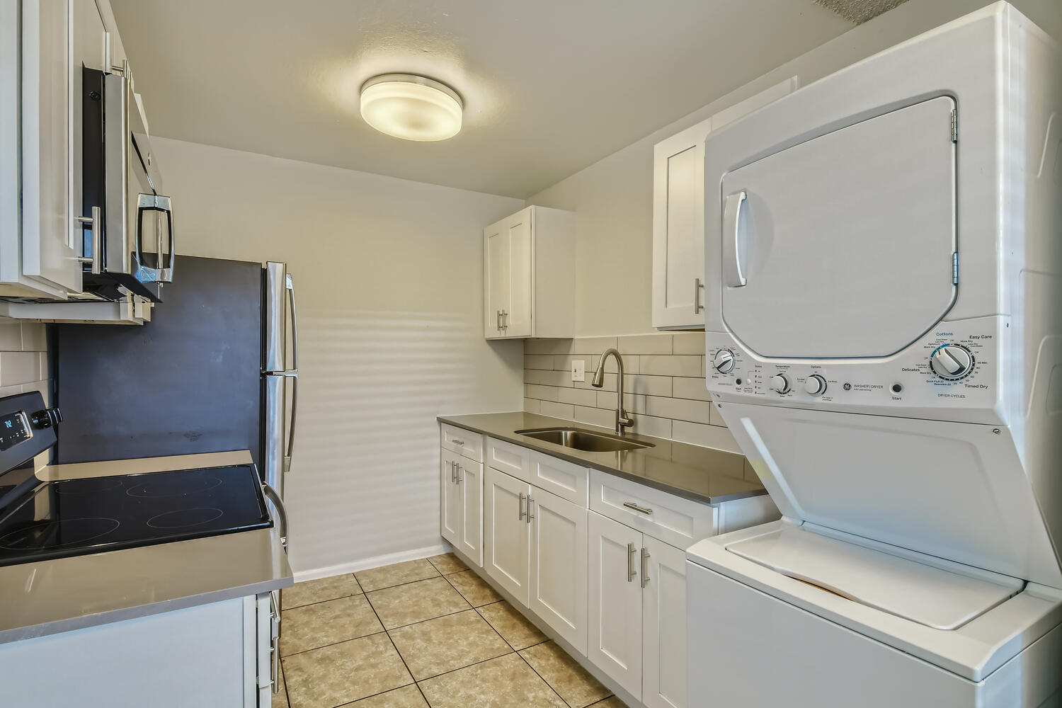 A kitchen with a washer and dryer and white shaker cabinets at Rise at the Palms. 