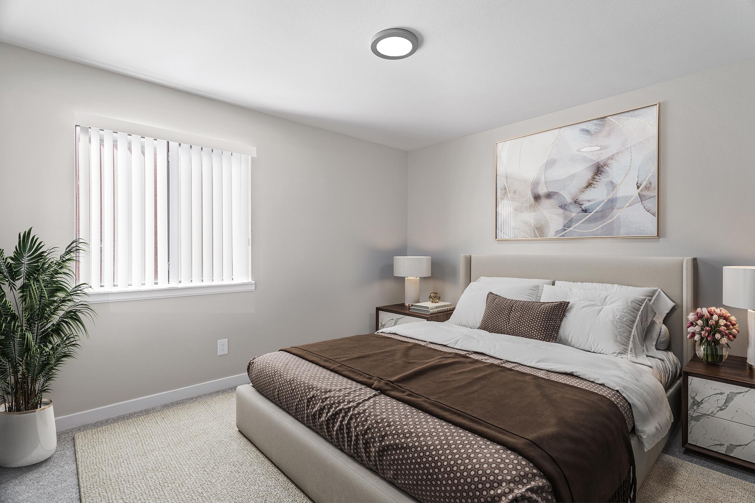 A cozy bedroom featuring a large bed with beige and brown bedding, two bedside tables with lamps, and a large piece of abstract artwork on the wall. A potted plant adds a touch of greenery, and window blinds allow natural light to filter into the room. The walls are painted in soft neutral tones.
