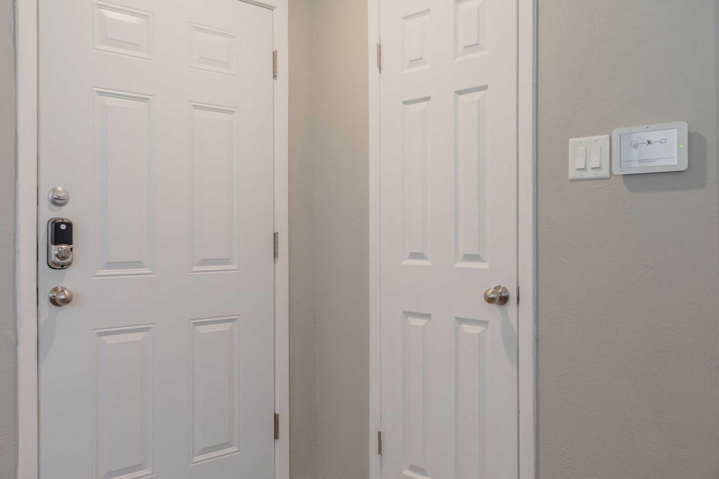 A view of a small hallway featuring a white front door on the left and another white door on the right. The walls are painted a light gray, and there is a light switch on the wall beside the right door. The overall appearance is clean and modern.