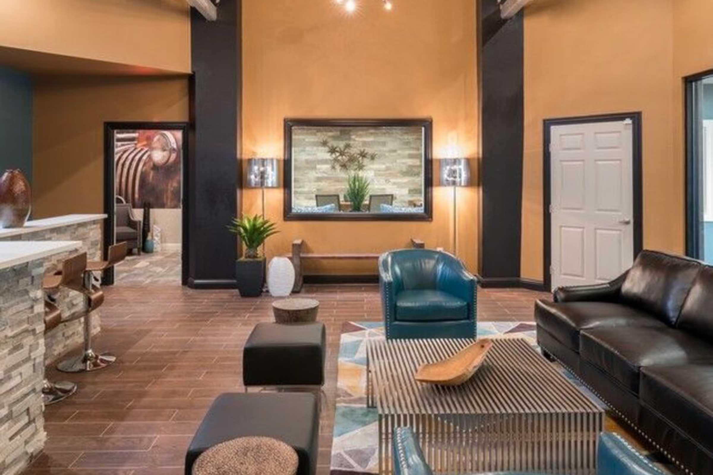 A modern interior with a stylish lounge area featuring a black leather sofa, blue accent chairs, and a patterned rug. A decorative coffee table sits on the floor, while floor-to-ceiling mirrors and wall art enhance the space's contemporary feel. Soft lighting creates a warm ambiance.