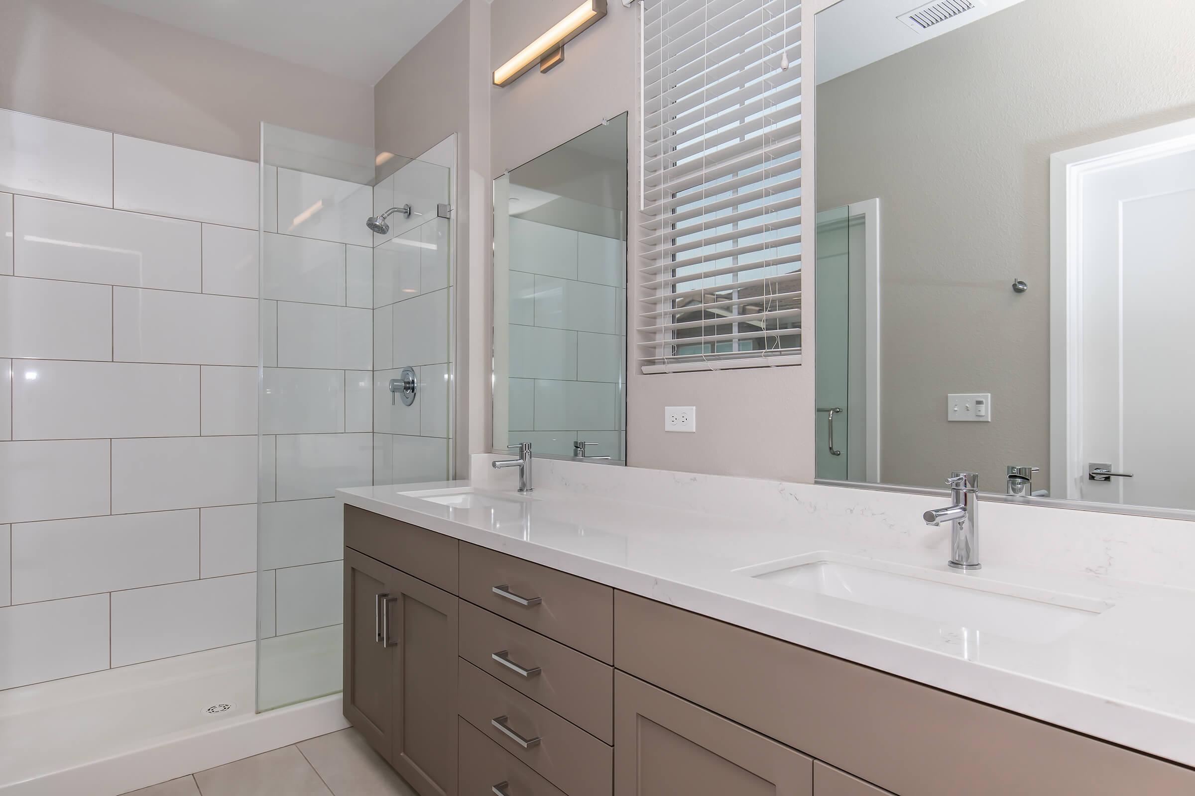 Apartments Near Fresno State in Fresno County, CA - Parador Townhomes - Bathroom With A Large Shower With A Glass Door, White Tile In The Shower, A Double Vanity, and Two Mirrors Over The Sinks