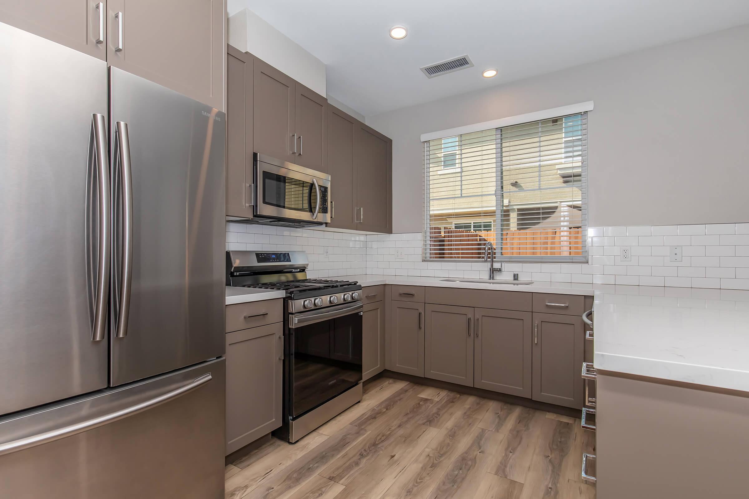 Apartments Near Fresno Pacific University In Fresno County, CA - Parador Townhomes - Spacious Kitchen with Stainless Steel Appliances, Designer Wood-Inspired Flooring, A Large Window, and White Tile Backsplash