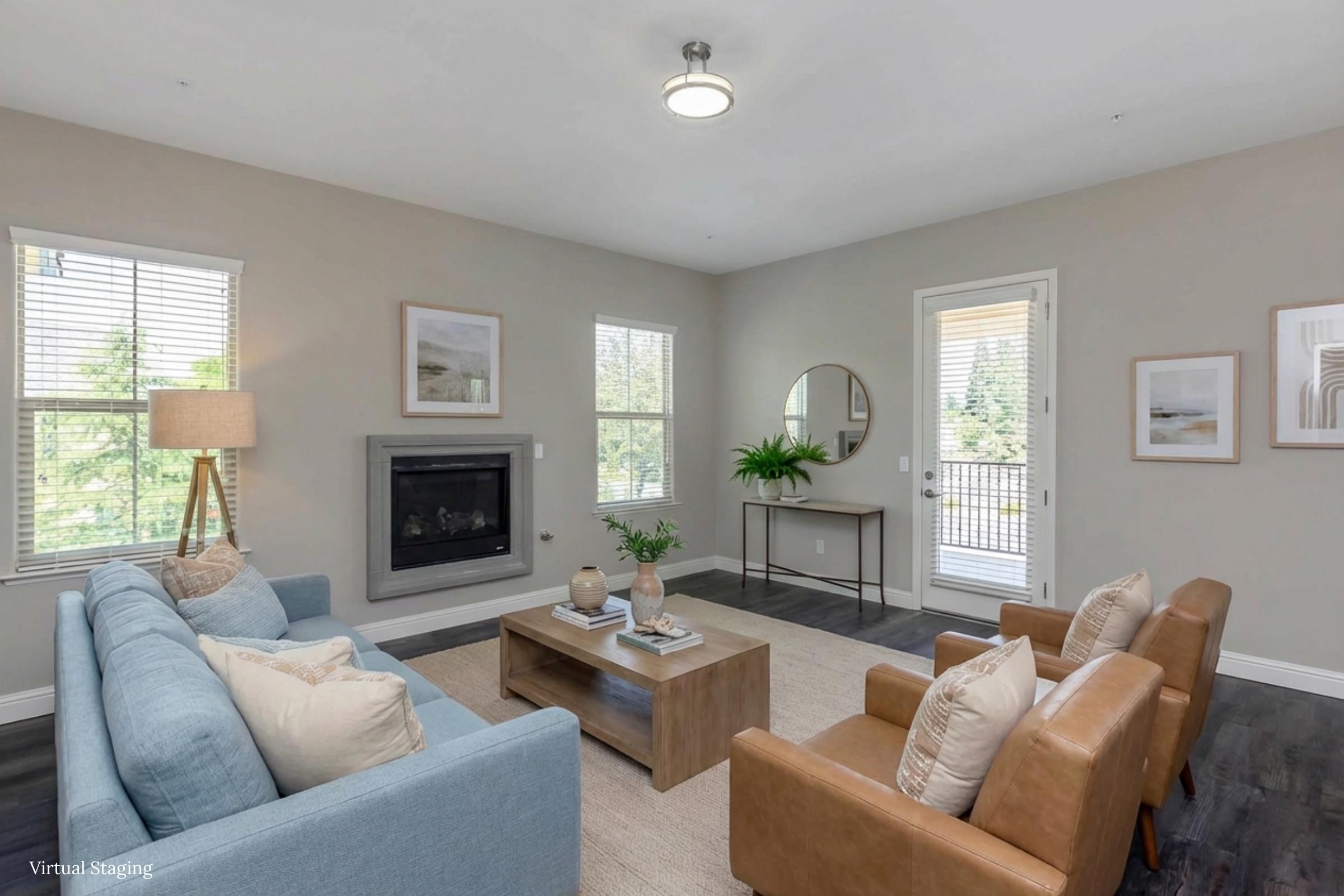 A cozy living room featuring a light blue sofa, two brown armchairs, and a wooden coffee table with decorative items. A modern fireplace is situated against the wall, and a large mirror reflects natural light from the windows. The walls are painted in neutral tones, creating a warm atmosphere.
