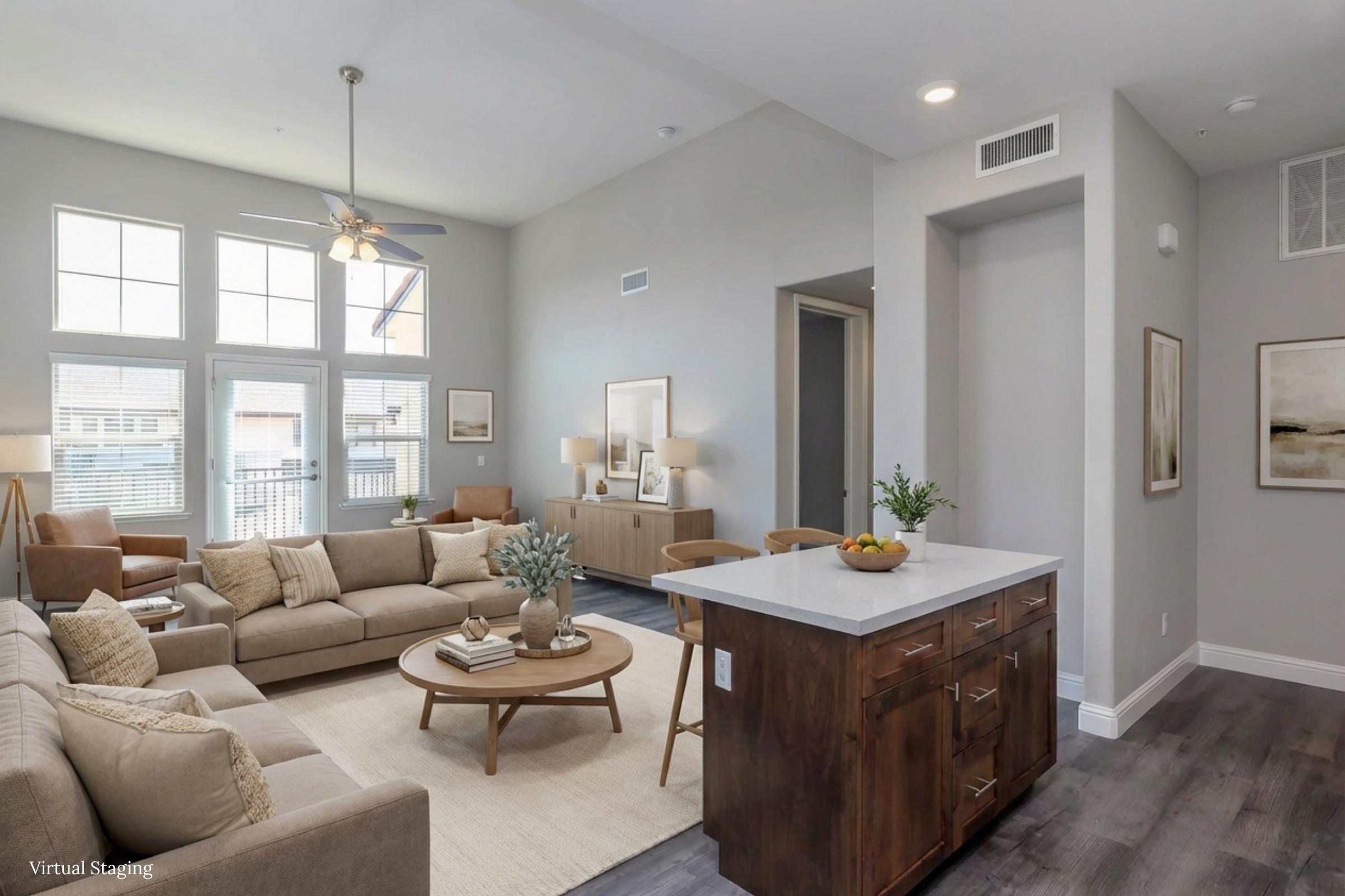 A modern, open-concept living room featuring a cozy sofa, coffee table, and decorative accents. Large windows allow natural light to fill the space, complemented by neutral decor. A kitchen island with bar seating is visible, creating a seamless flow between the living and dining areas.